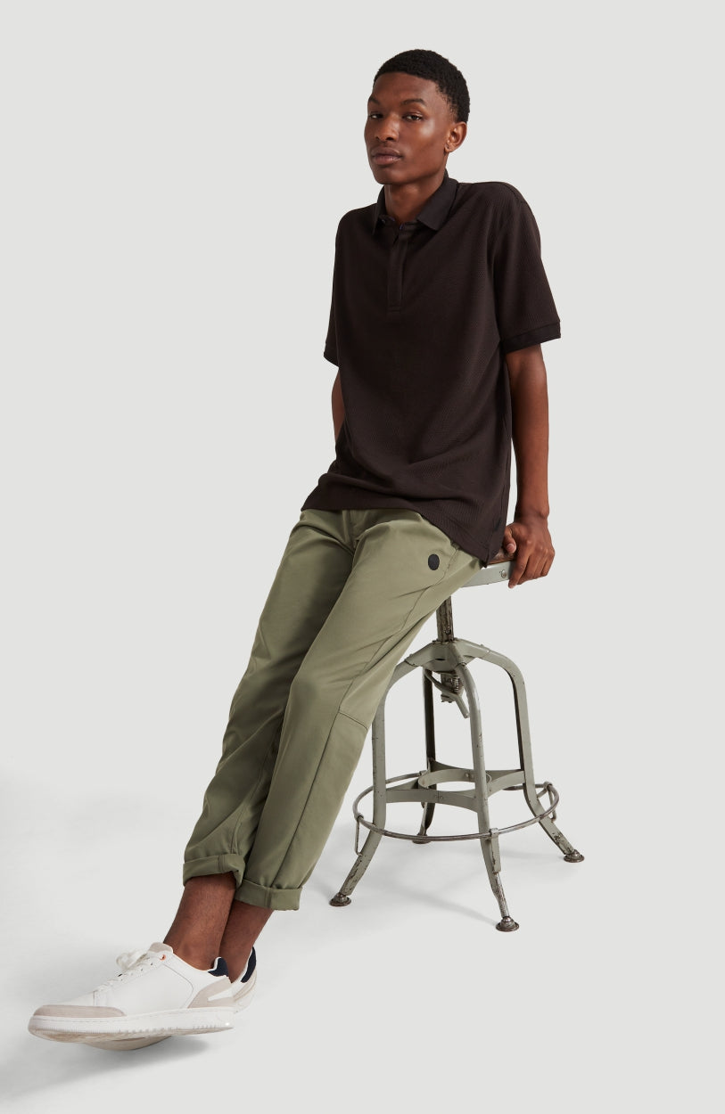 Hybrid Waffle Polo Shirt Poloshirt für Herren, schwarz, getragen am Model auf einem Hocker in Gesamtansicht