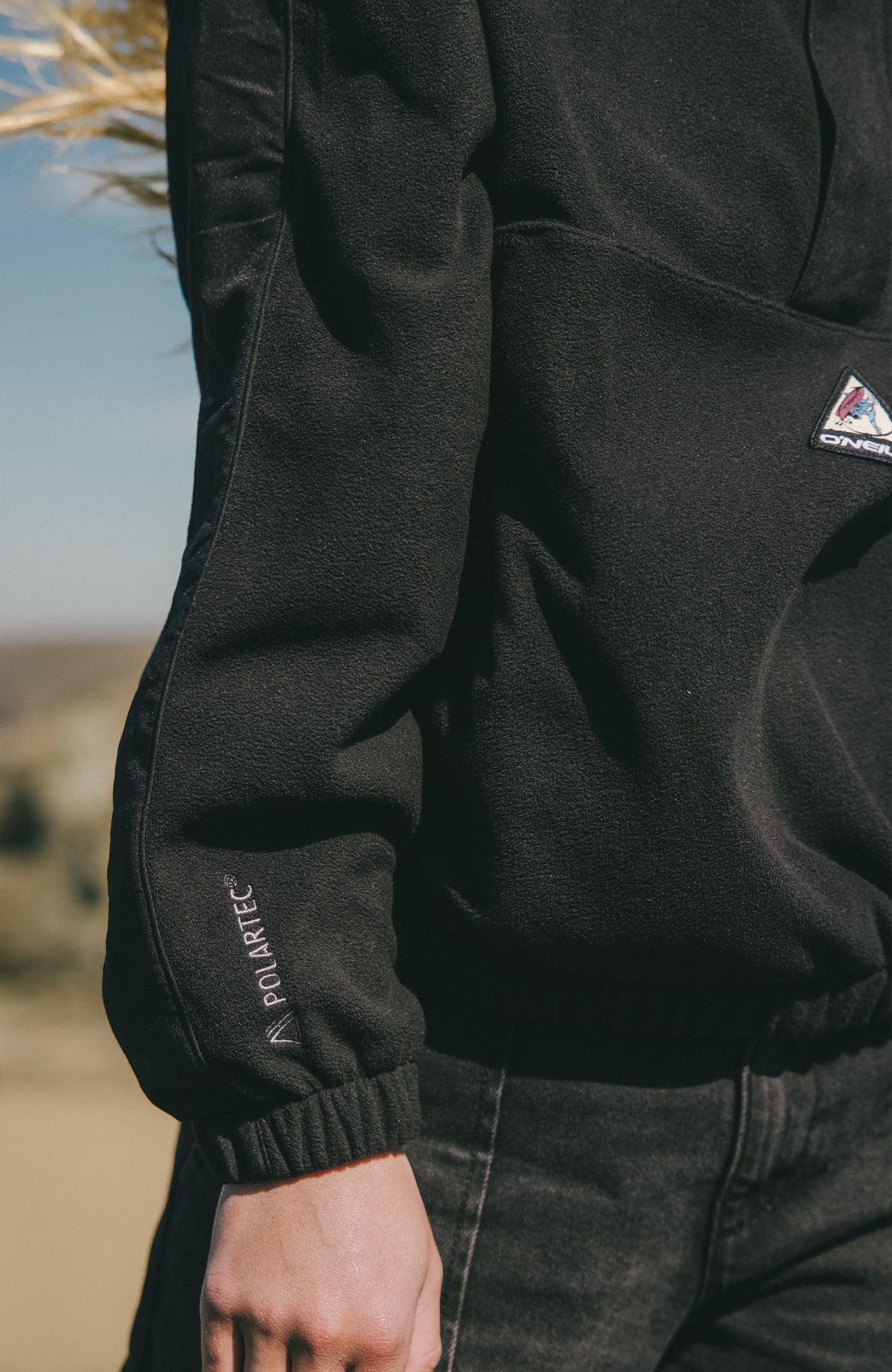 Nahaufnahme des Ärmelsaums mit Logo-Stickerei am schwarzen FWC'Play Polartec® Fleecepullover