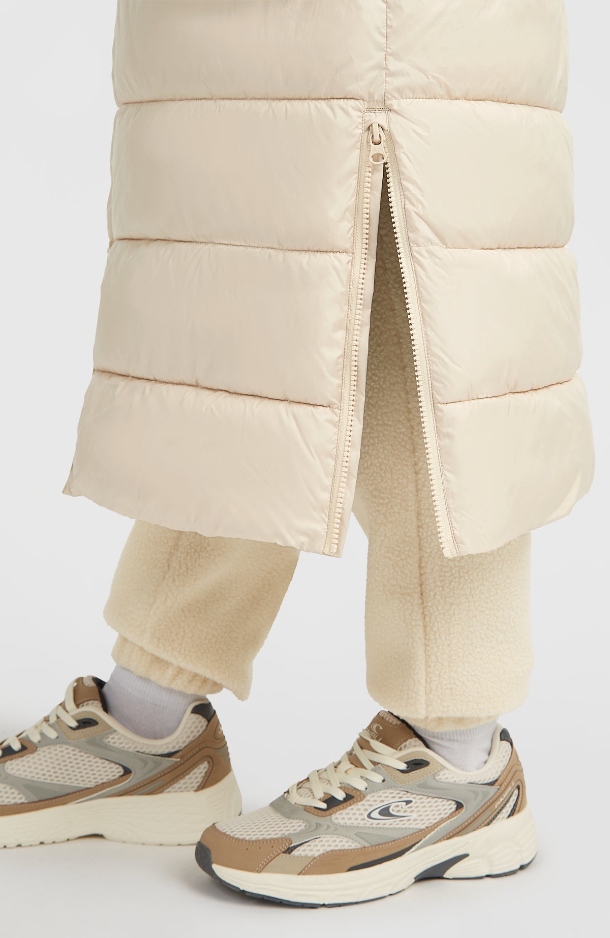 Nahaufnahme vom unteren Saum und seitlichen Reißverschluss der beigen Lange Must-Have Steppjacke