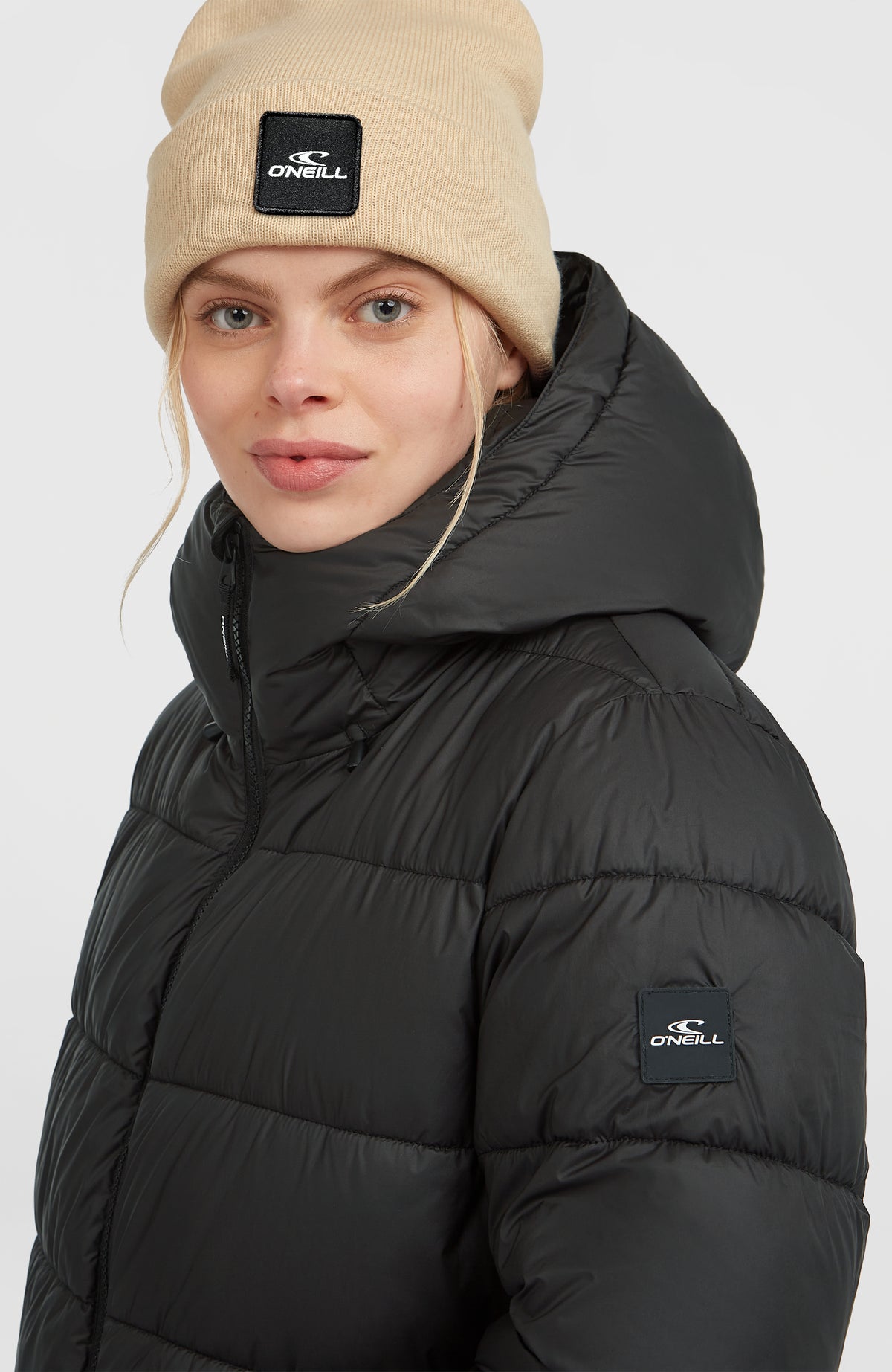 Lange Must-Have Steppjacke für Damen, schwarz, Nahaufnahme am Model mit Logo-Patch am Ärmel