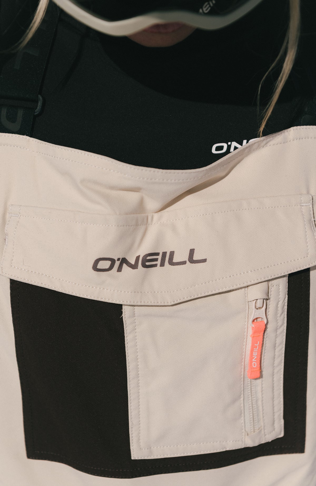 Nahaufnahme des Latzbereichs der beigen FWC'Peak Bib Skihose mit Brusttasche und Logo