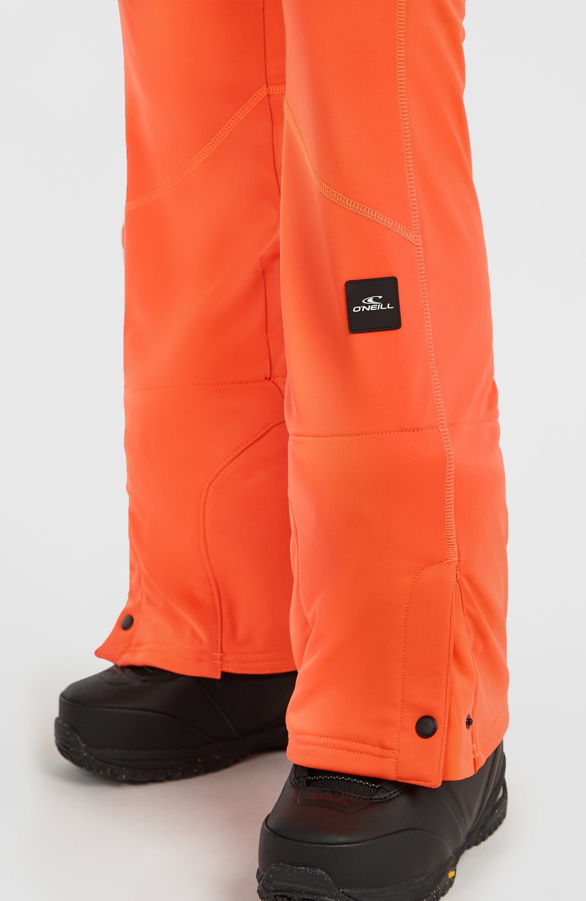 Nahaufnahme des unteren Hosenbeins der roten FWC'Cruz Softshell-Skihose mit Logo-Patch und Druckknöpfen