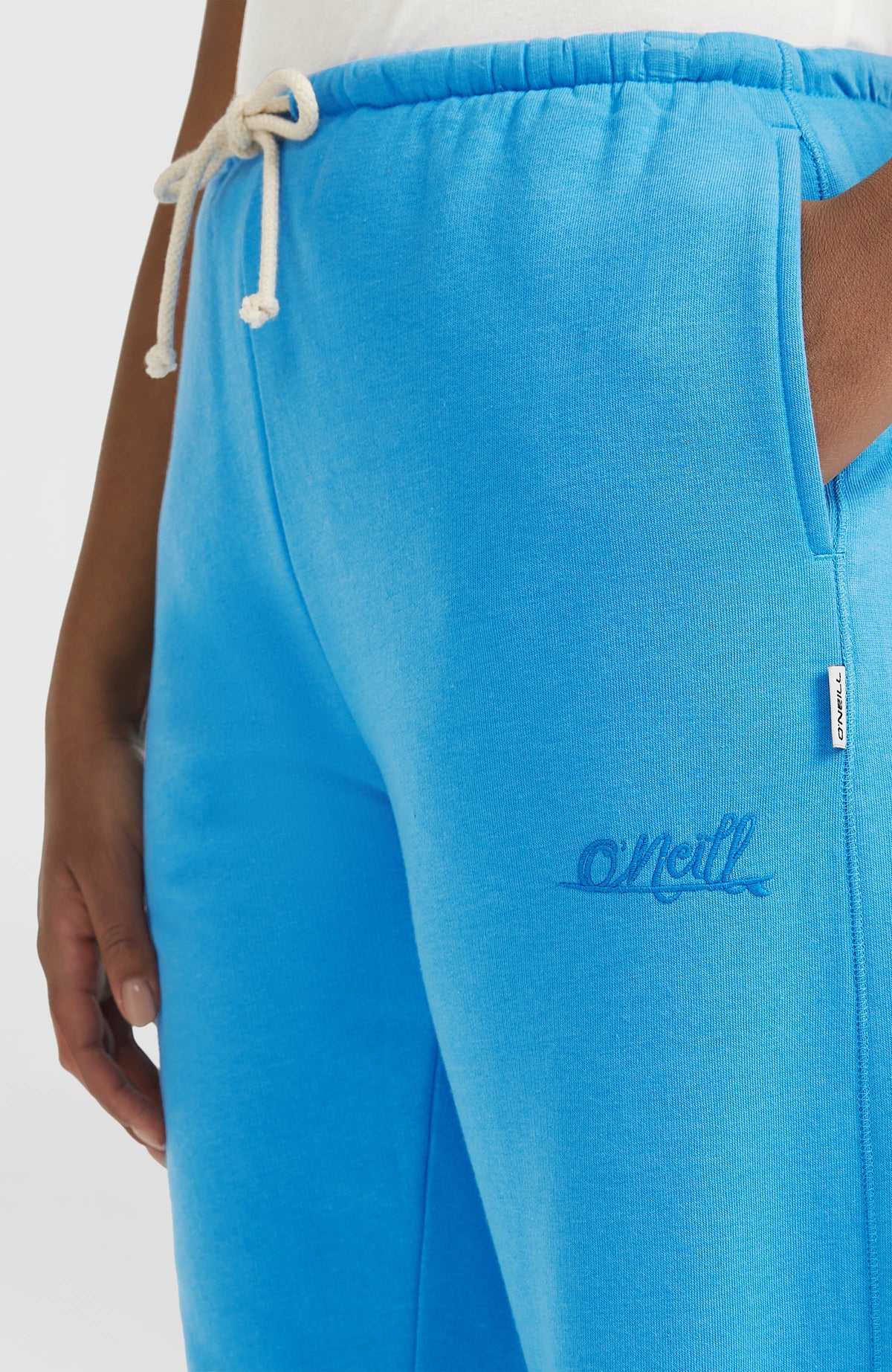 Nahaufnahme der blauen Essentials Script Jogginghose am Model, Seitentasche und Logo-Stickerei
