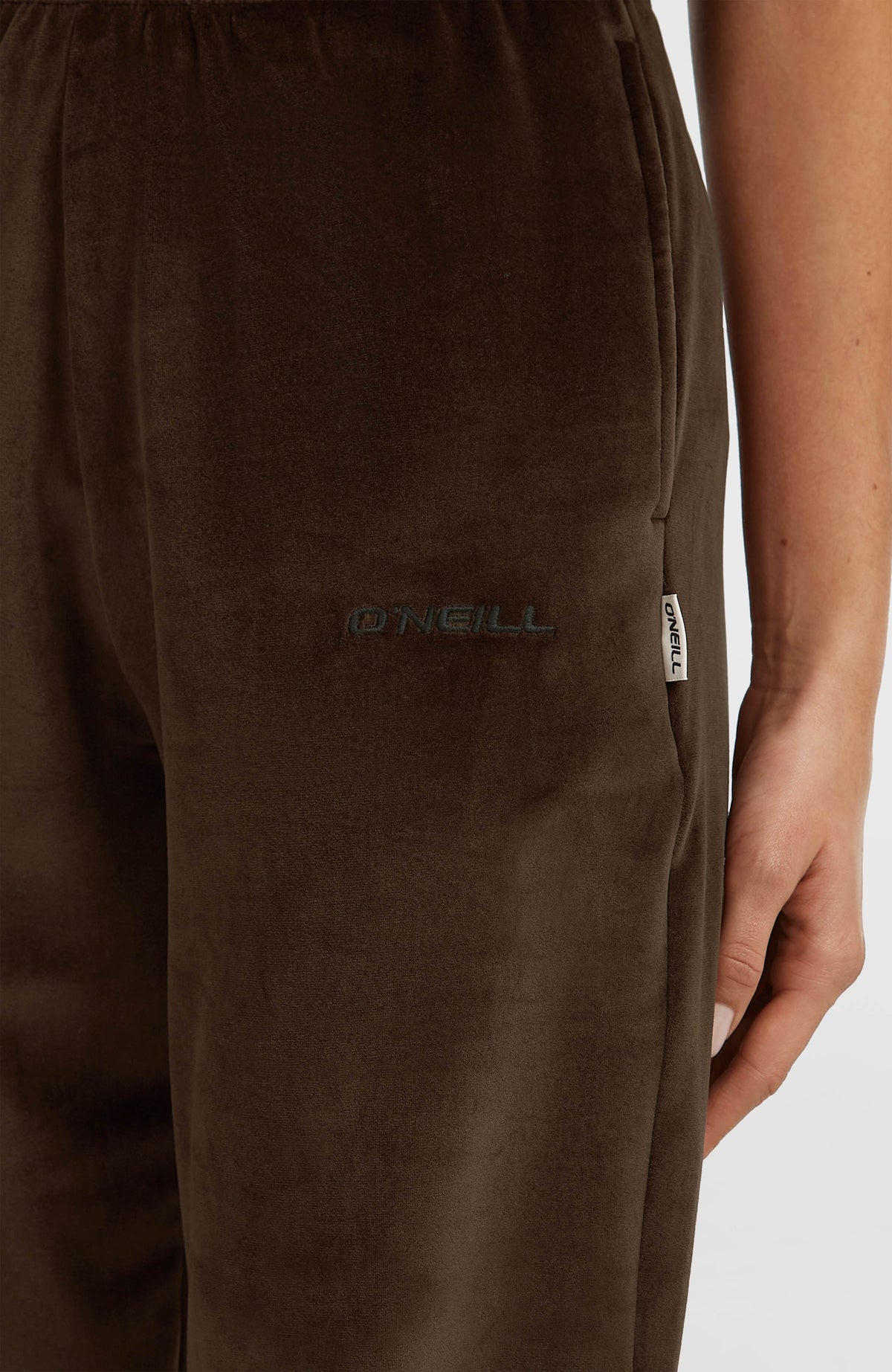 Nahaufnahme der braunen FWC'Cruz Velour Jogginghose am Model, gestickter Logo-Schriftzug und Label-Fähnchen