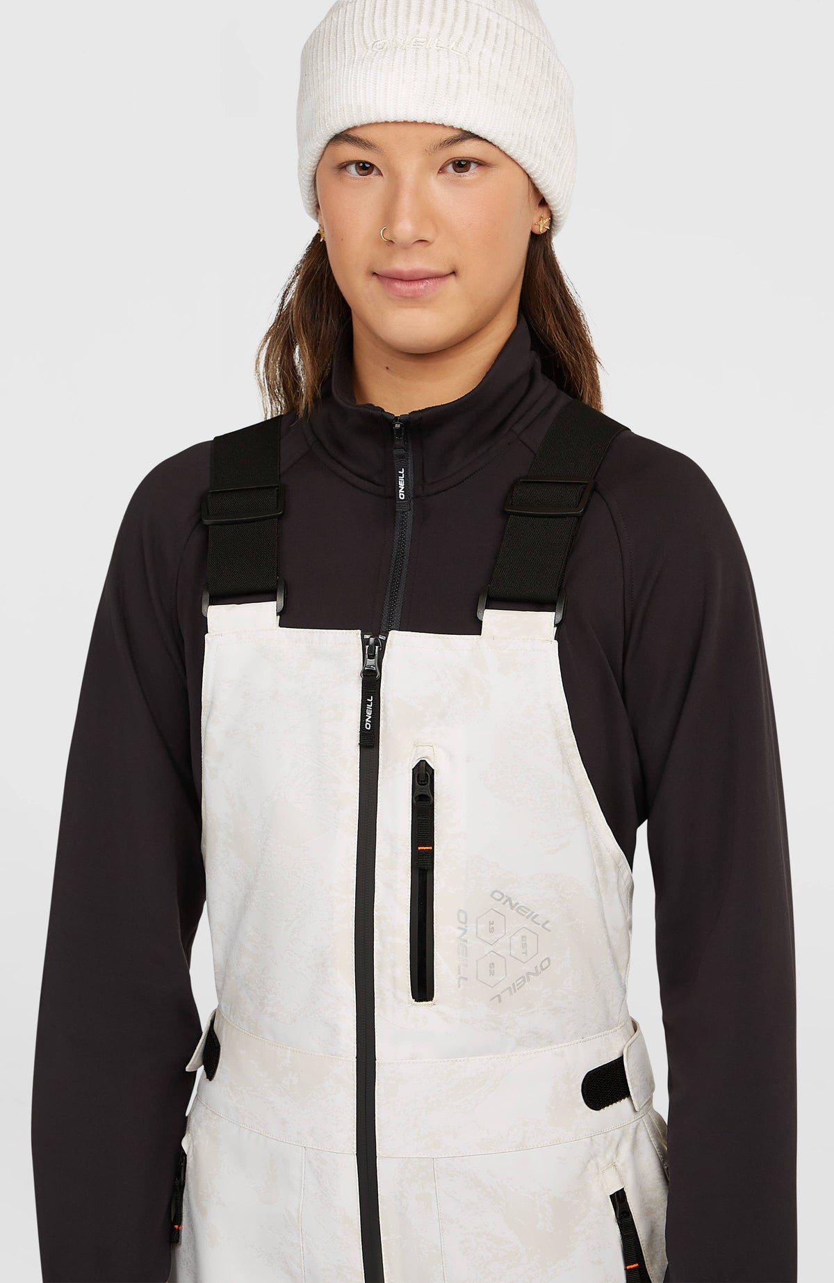 Nahaufnahme des Latzbereichs der weißen FWC'Peak Bib Skihose für Damen mit Reißverschlusstasche