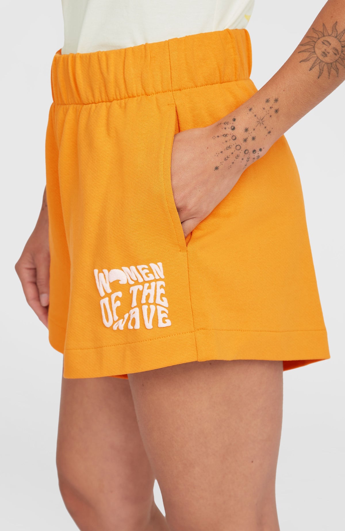 Women of the Wave Sweatshorts für Damen, orange mit Logo-Print in Weiß, Nahaufnahme der Seitentasche am Model