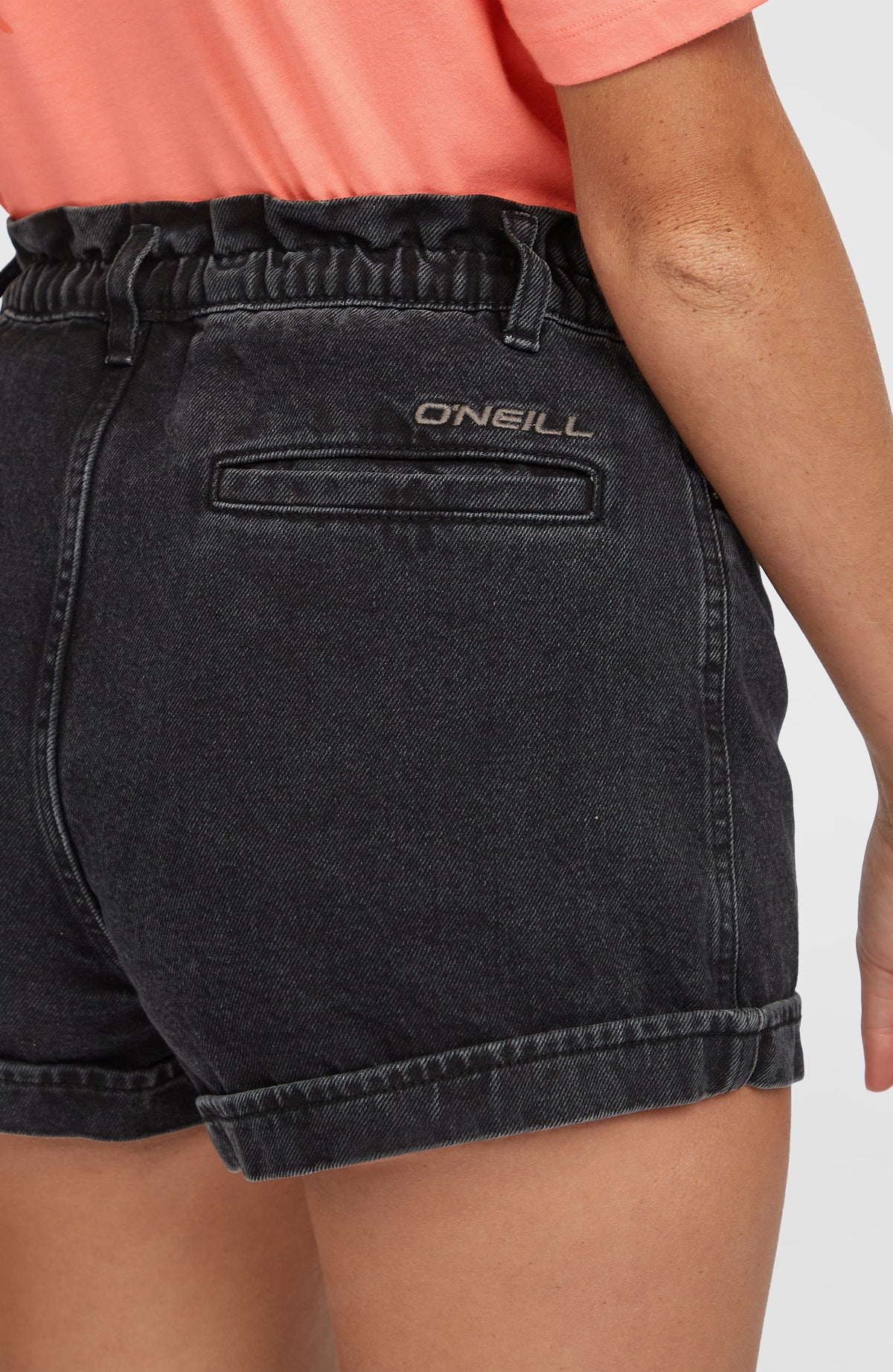 Nahaufnahme der Tasia Paperbag Shorts, schwarz, getragen am Model, Paspeltasche hinten mit Logo-Stickerei