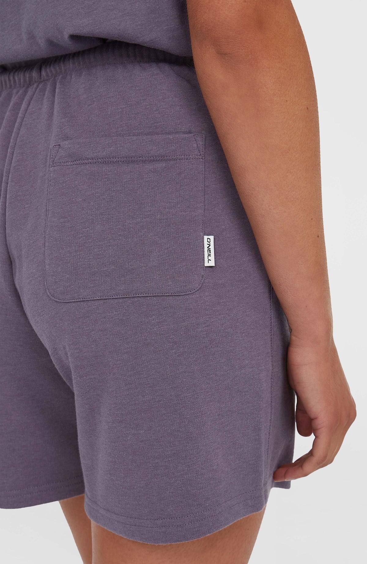 Nahaufnahme der Gesäßtasche mit gewebtem Logo-Label an den lila Essentials O'Neill Script Sweatshorts