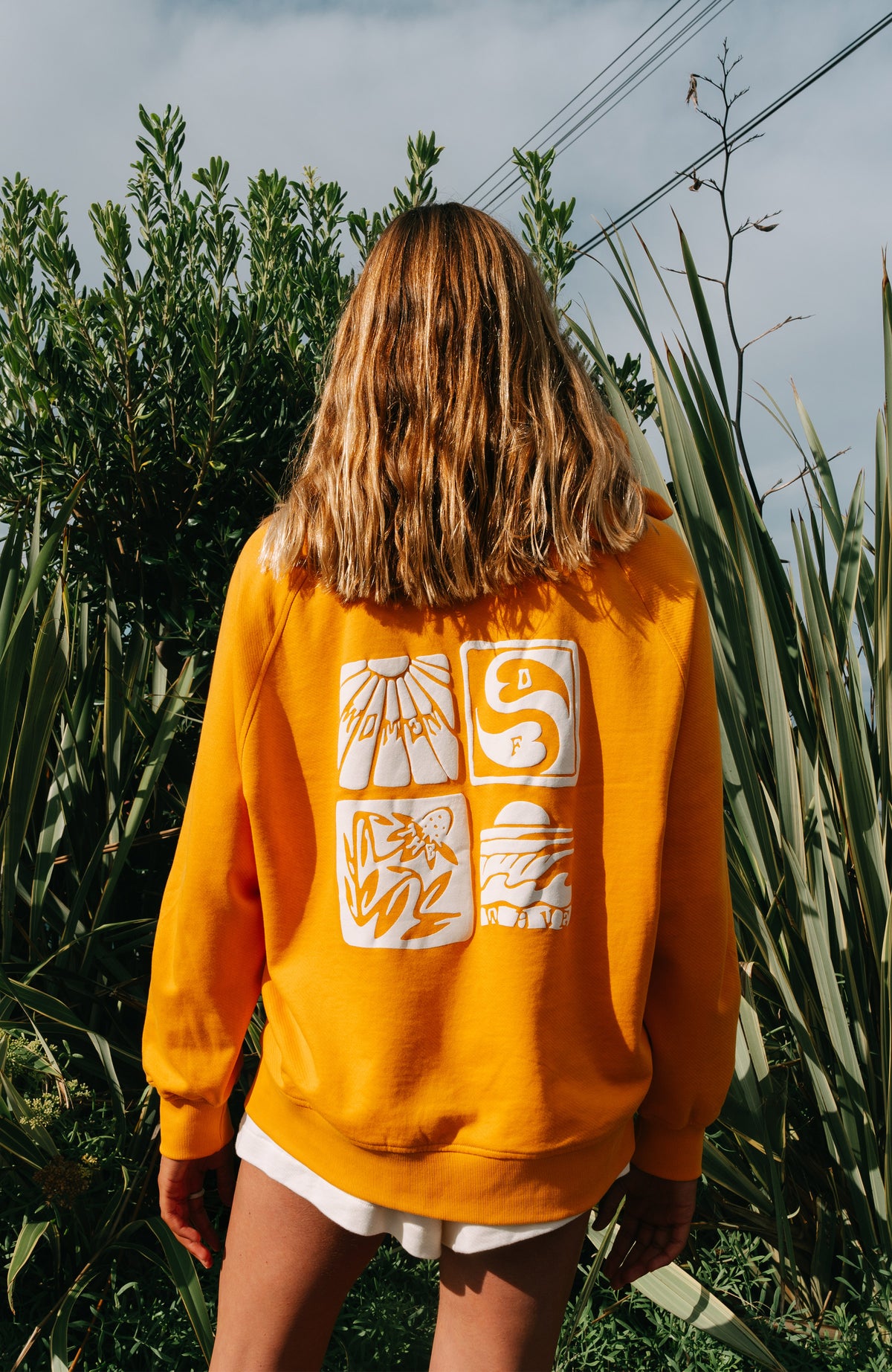 Women of the Wave Hoodie, orange mit Grafik-Print in Weiß, Rückansicht im Freien vor Pflanzen