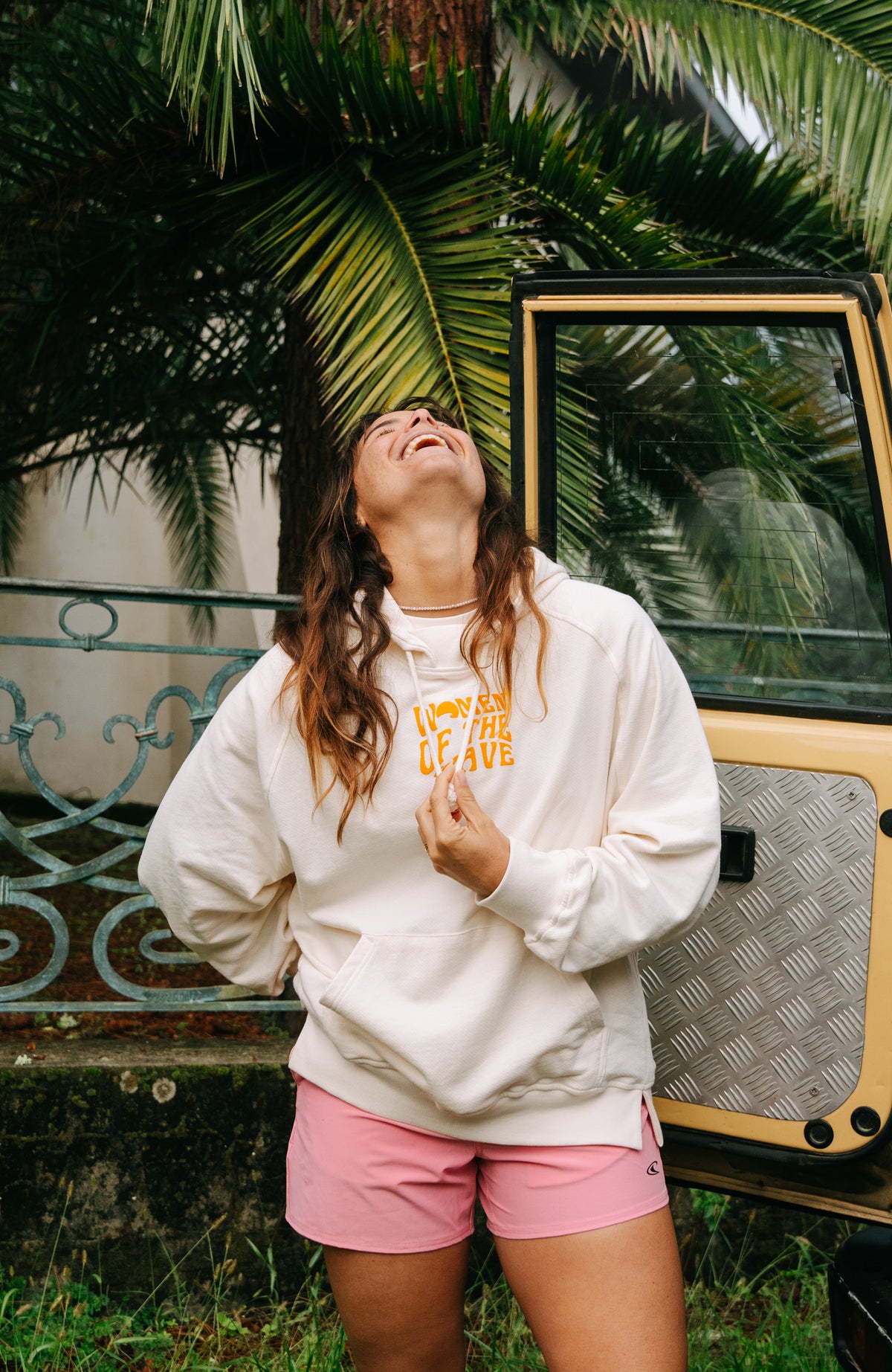 Women of the Wave Hoodie für Damen, beige mit Grafik-Print in Orange, getragen am Model neben einem Geländewagen
