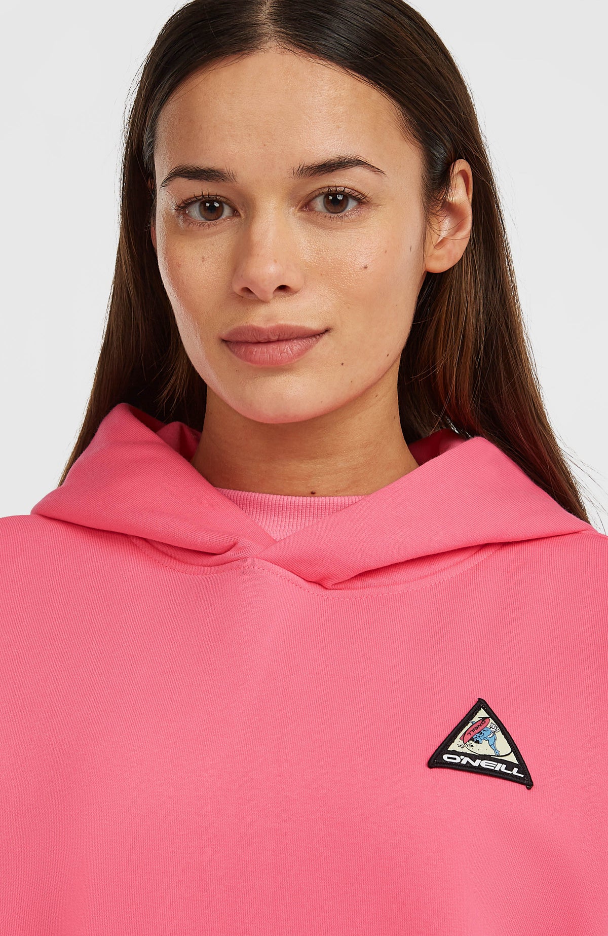 Nahaufnahme des pinken FWC'Play Hoodie für Damen mit überlappendem Kragen und dreieckigem Logo-Badge
