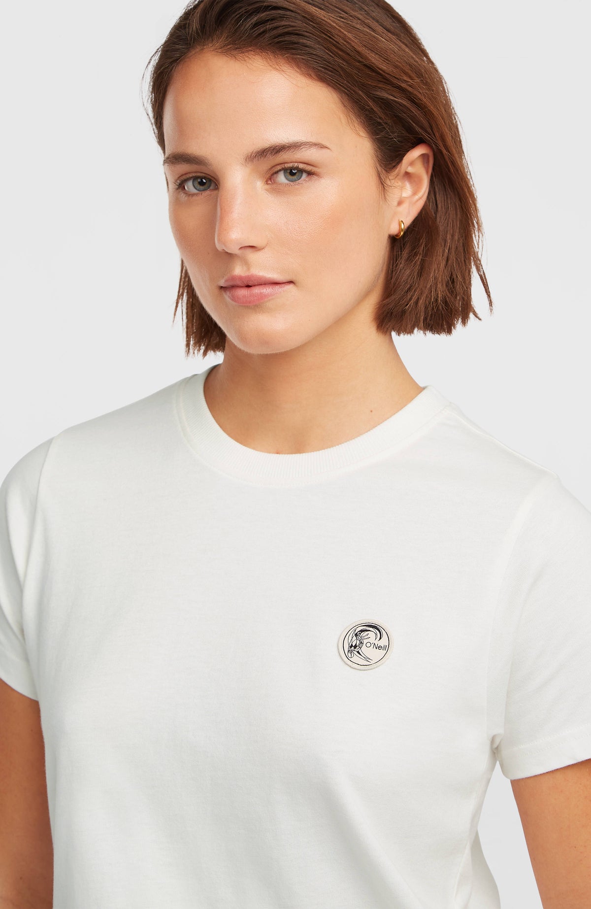 Nahaufnahme des runden Logo-Badges auf der Brust des weißen O'Riginals Badge T-Shirts am Model