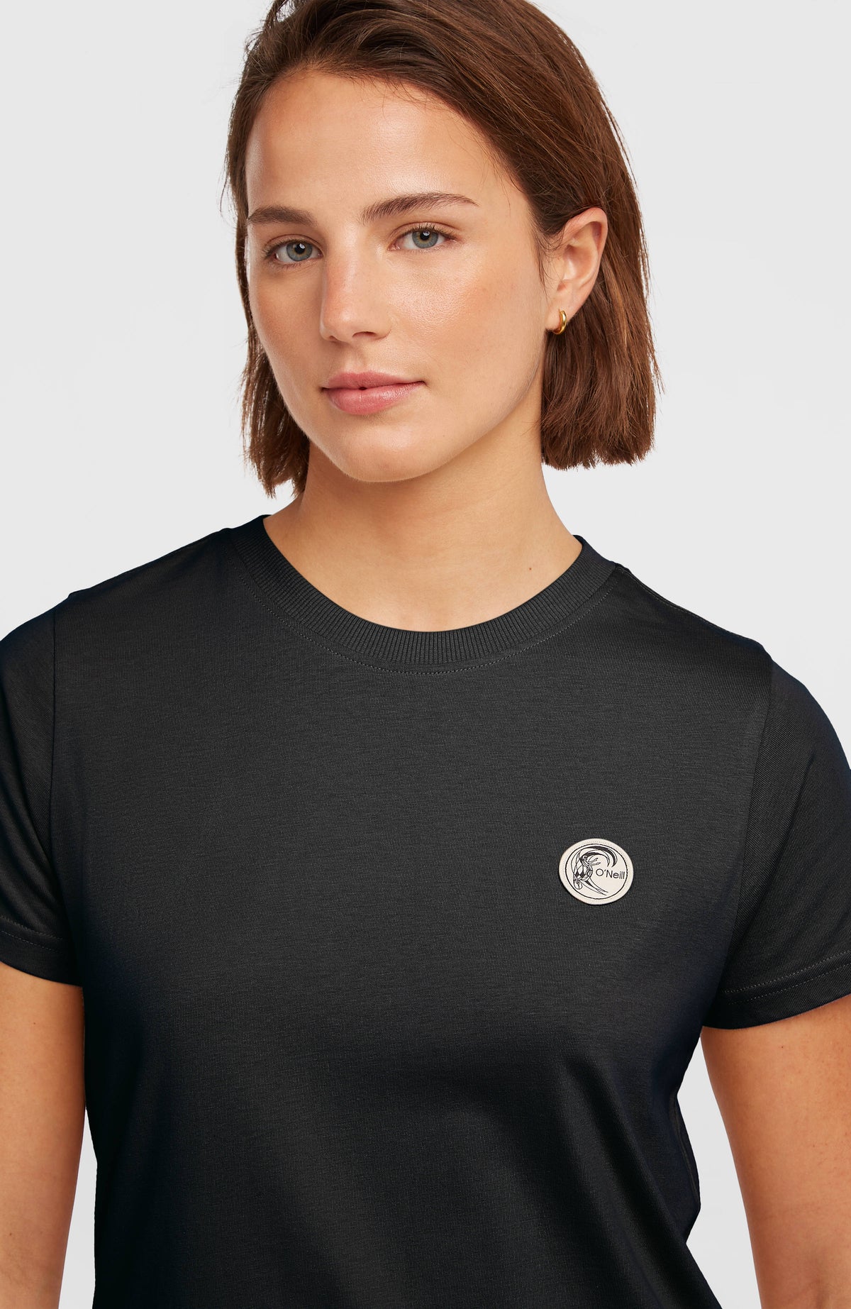 Nahaufnahme des O'Riginals Badge T-Shirt für Damen in Schwarz mit rundem Logo-Badge und geripptem Rundhalsausschnitt