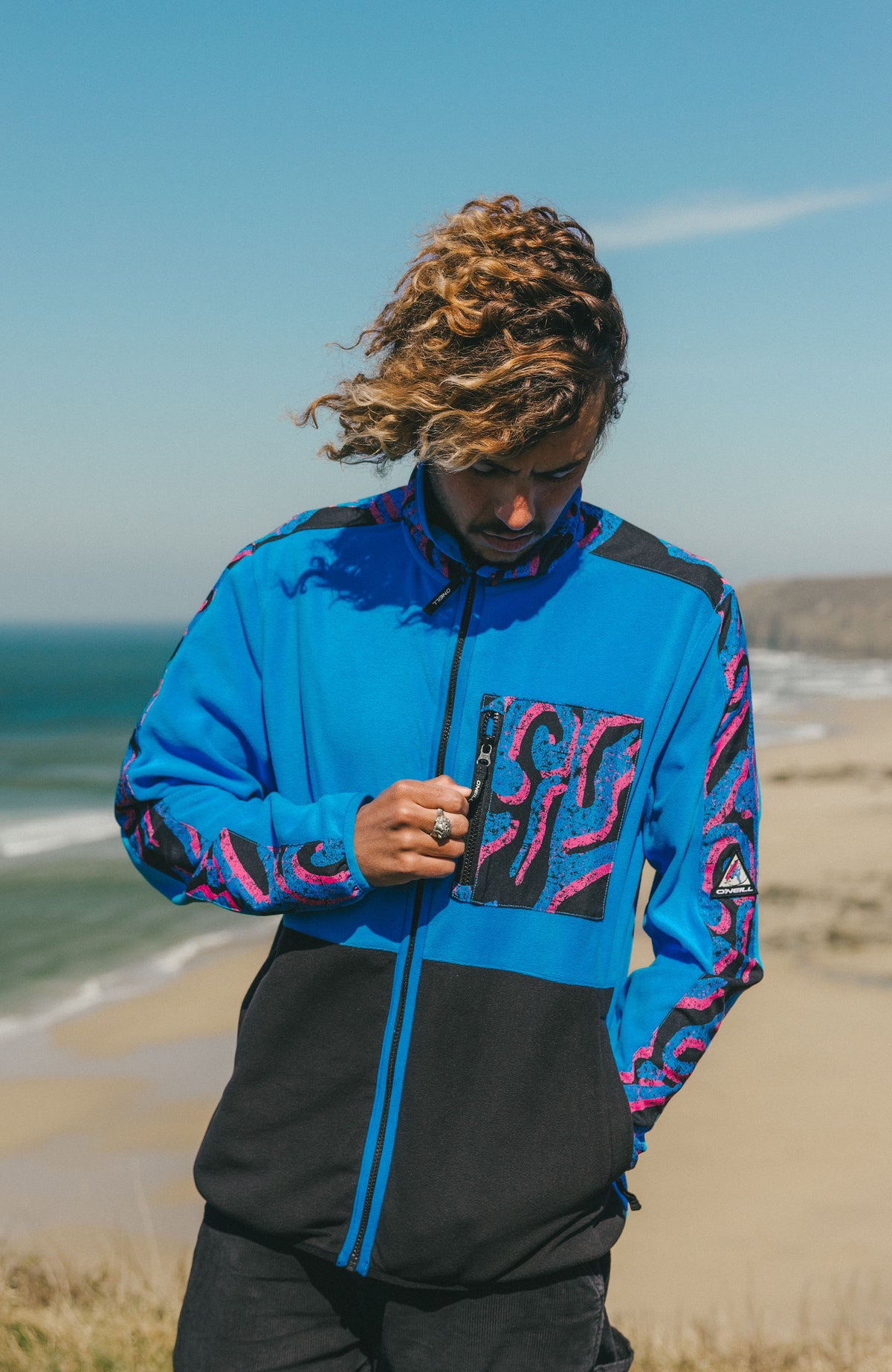 FWC'Play Polartec® Fleecejacke für Herren, pink mit Muster in Blau und Schwarz, am Strand mit Reißverschlusstasche