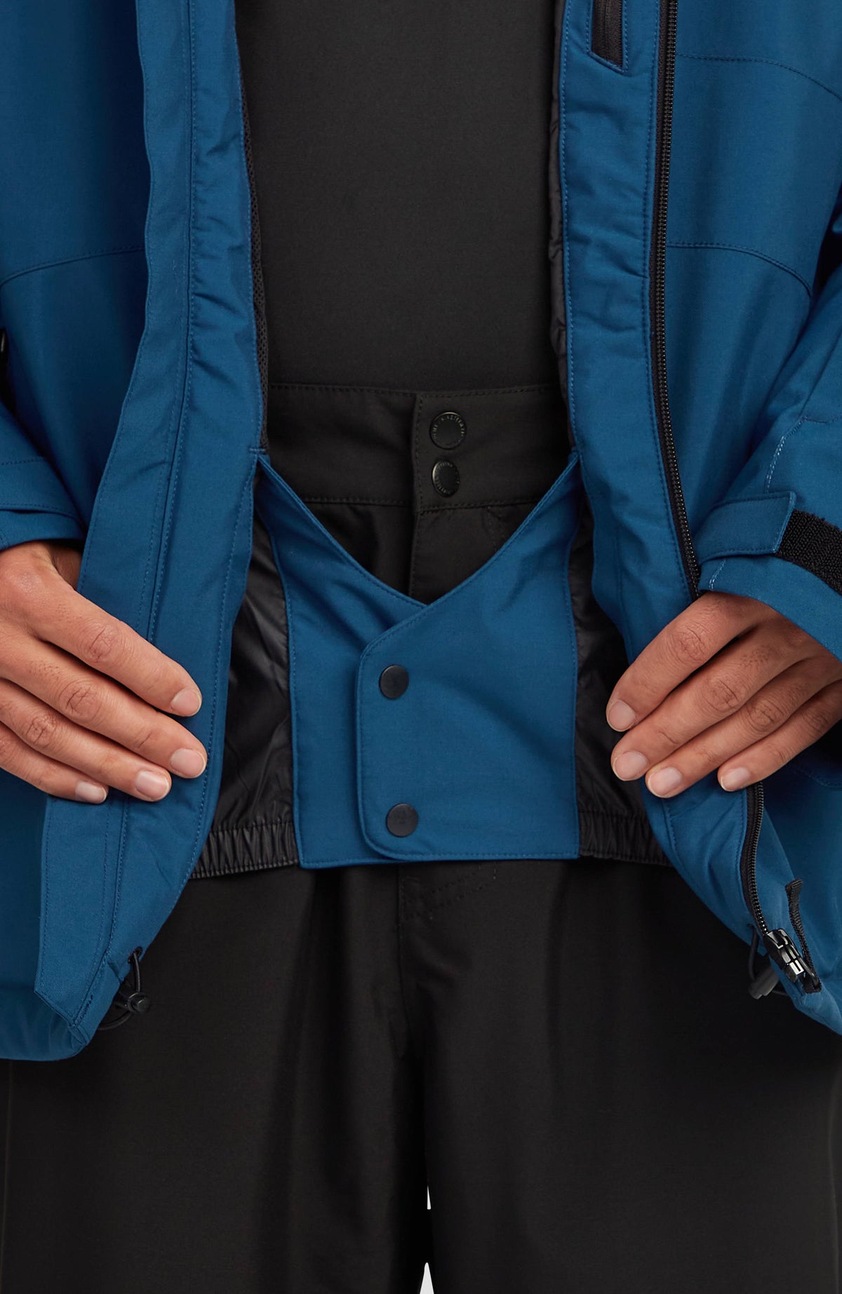 Nahaufnahme des Schneefangs mit Druckknöpfen der blauen FWC'Cruz Skijacke