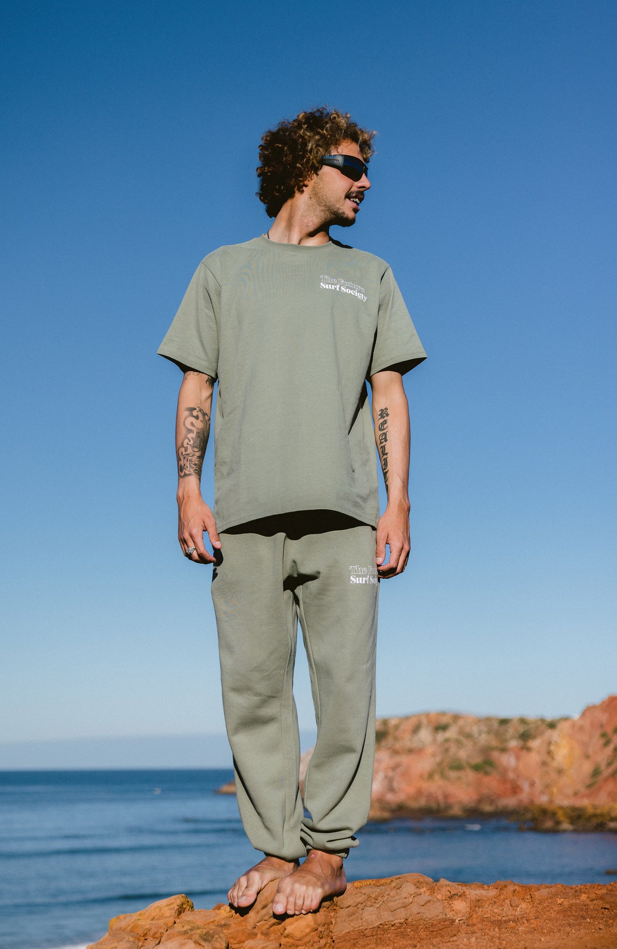 Future Surf Society Jogginghose für Herren in Grün, getragen am Model auf Felsen an der Küste