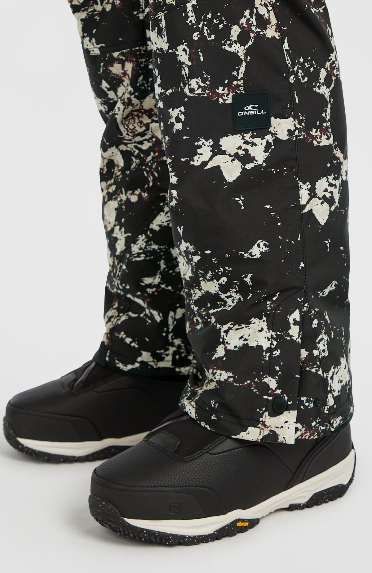 Nahaufnahme des unteren Hosenbeins der schwarzen FWC'Cruz Skihose mit Allover-Muster in Beige und Logo-Patch