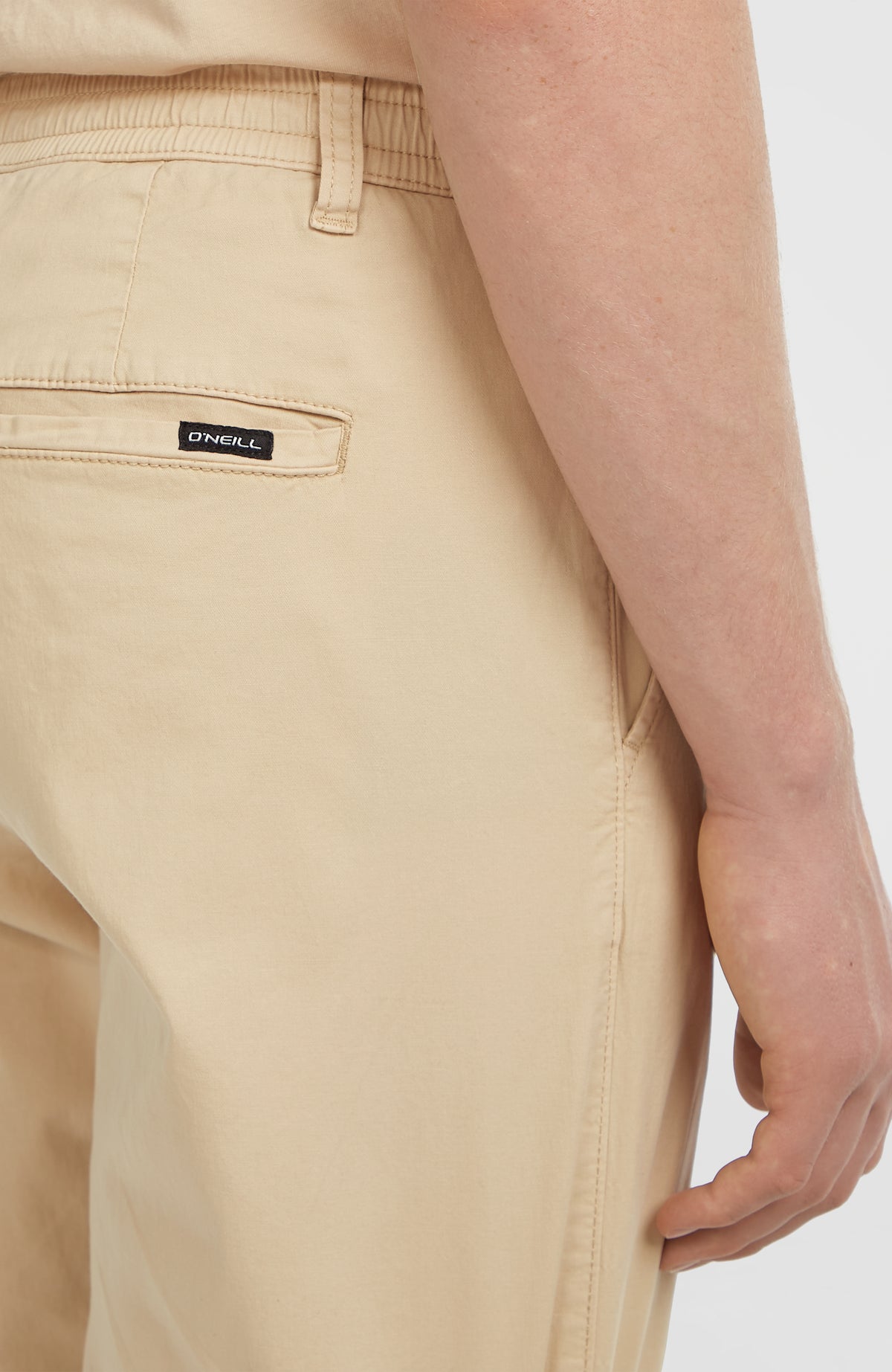Nahaufnahme der beigen Essentials Chino-Hose, elastischer Bund und Paspeltasche mit Logo-Patch
