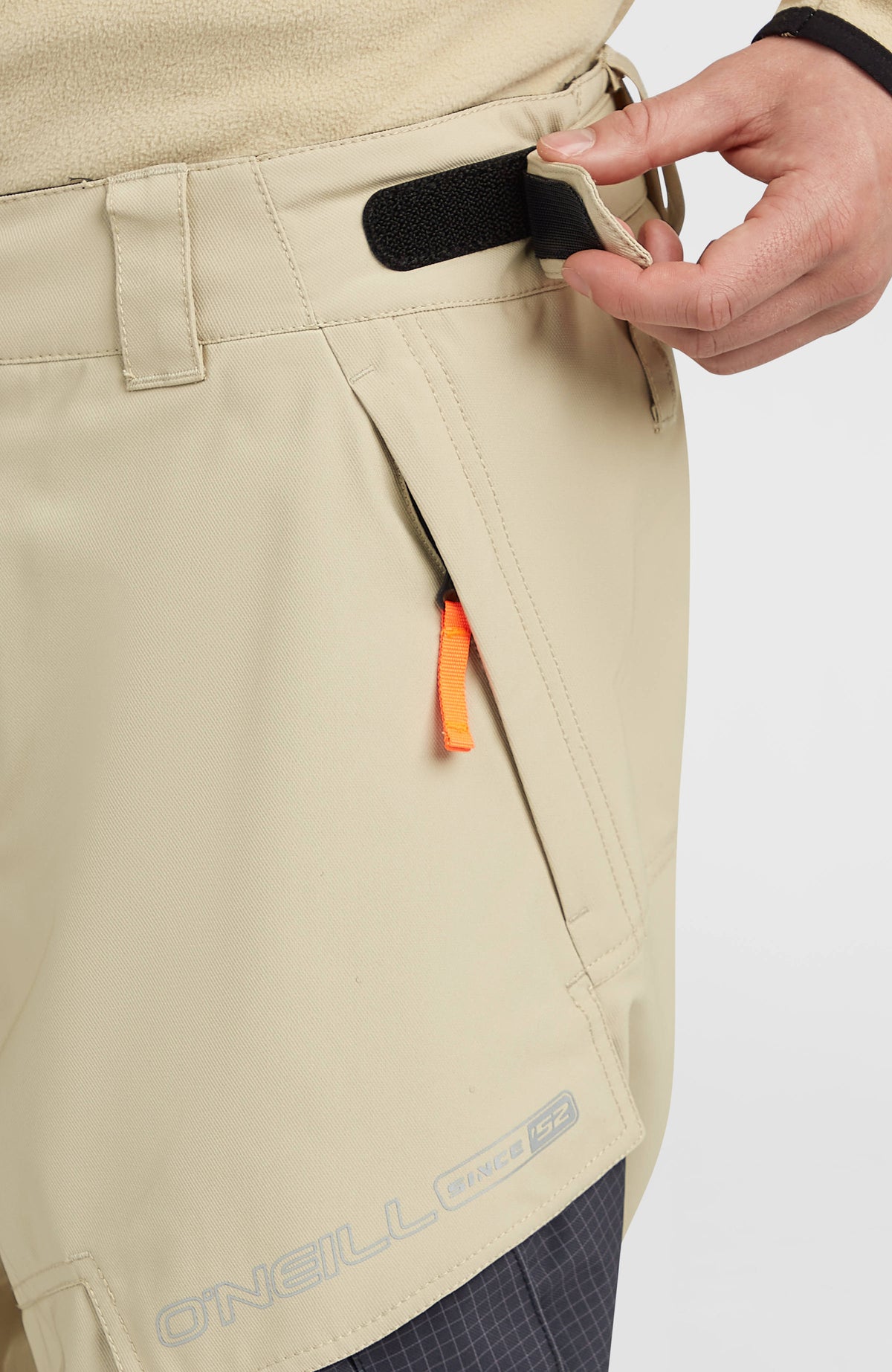 Nahaufnahme des Bundes mit Klettverschlussriegel und Reißverschlusstasche der beigen FWC'Peak Cargo-Skihose