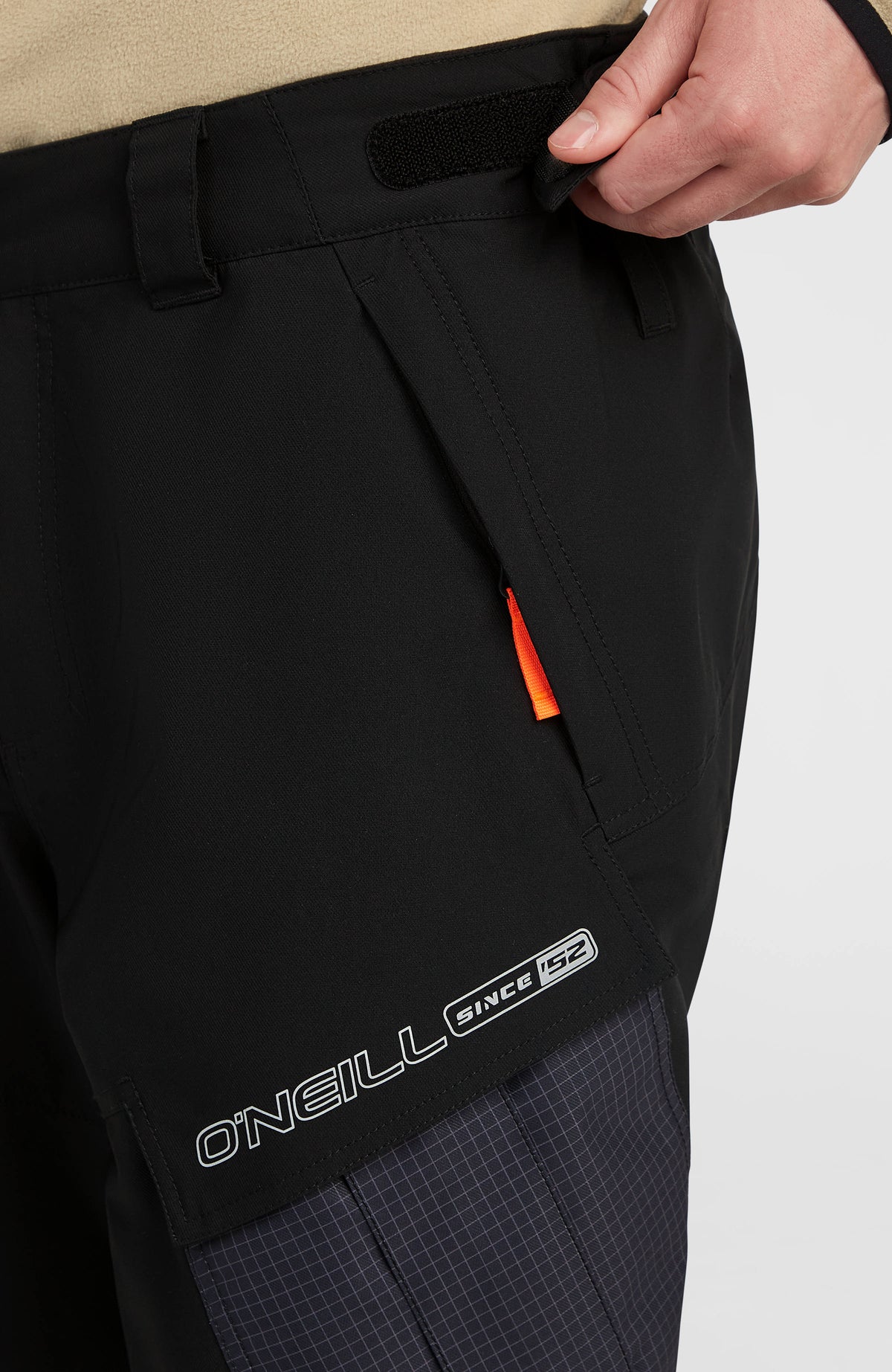 Nahaufnahme der seitlichen Cargotasche mit Logo-Schriftzug und Zuglasche der schwarzen FWC'Peak Cargo-Skihose