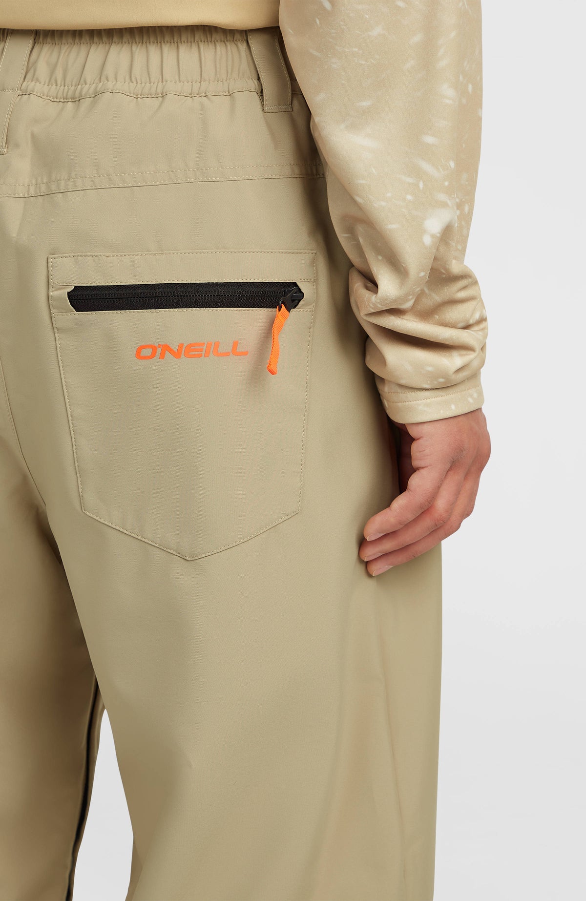 Nahaufnahme der hinteren Reißverschlusstasche mit Logo-Schriftzug der beigen FWC Oversized Ski- und Snowboardhose