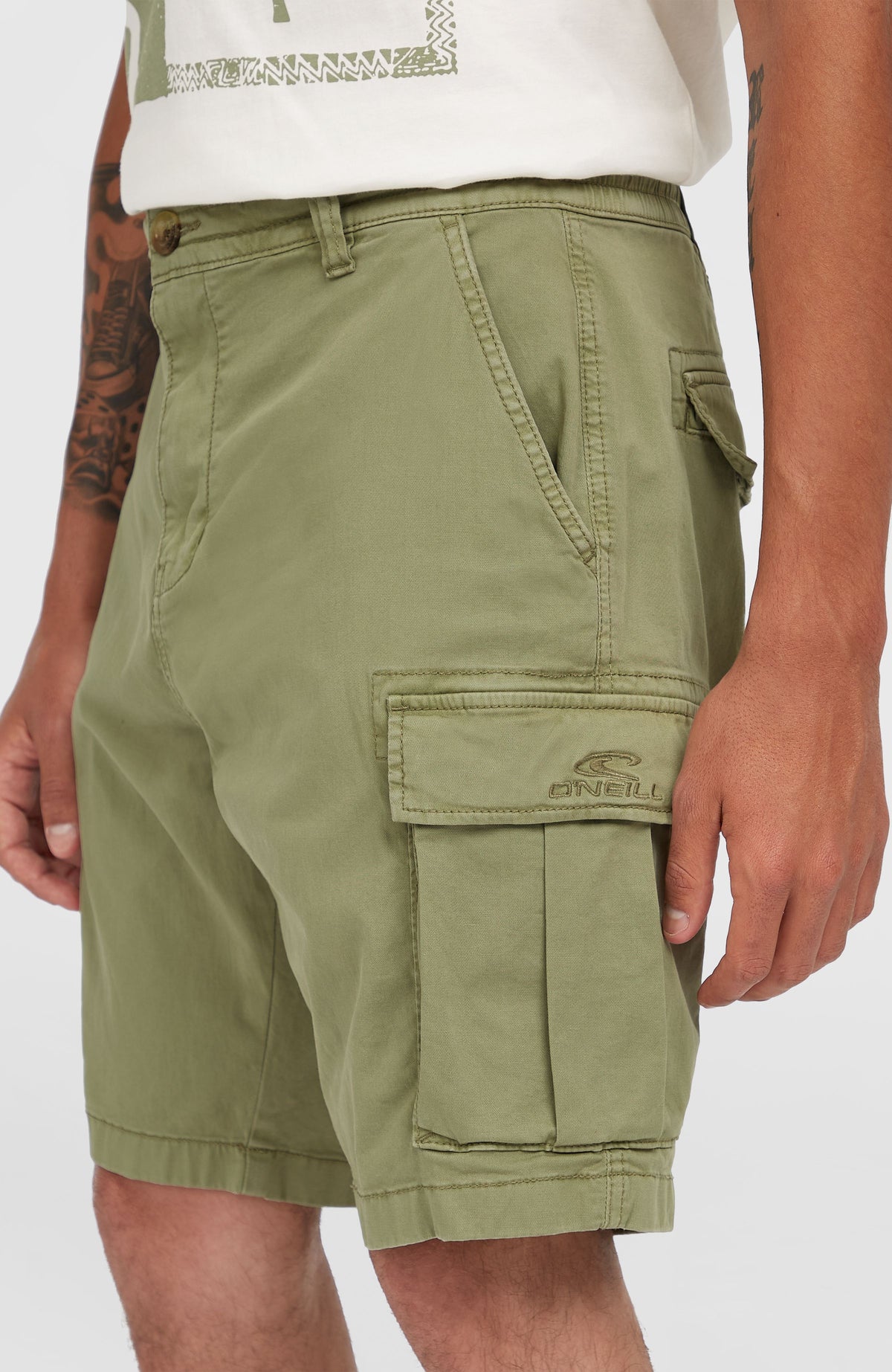 Nahaufnahme der seitlichen Tasche mit Logo-Stickerei an den grünen Essentials Cargo-Shorts am Model