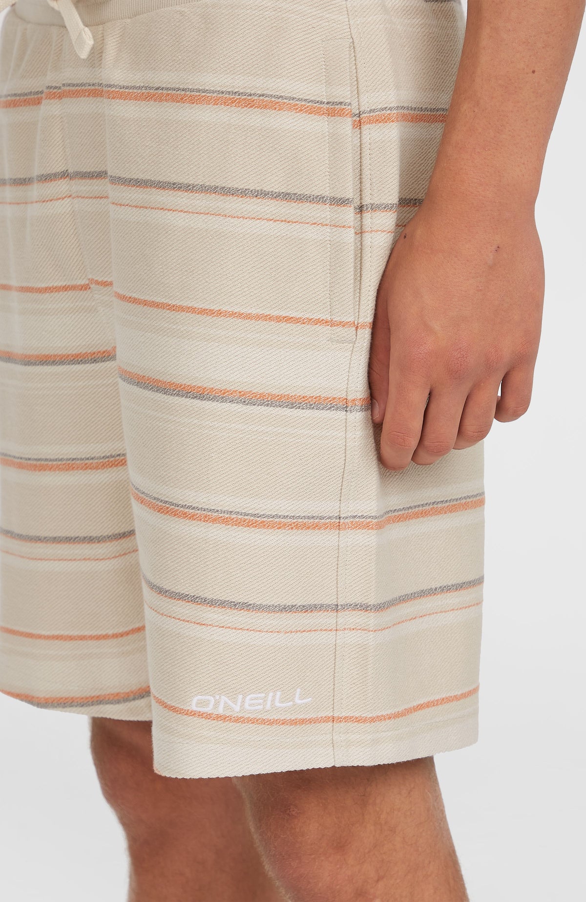 Nahaufnahme der beigen Bavaro Shorts mit Streifenmuster in Orange und Grau, weißer Logo-Schriftzug am Saum