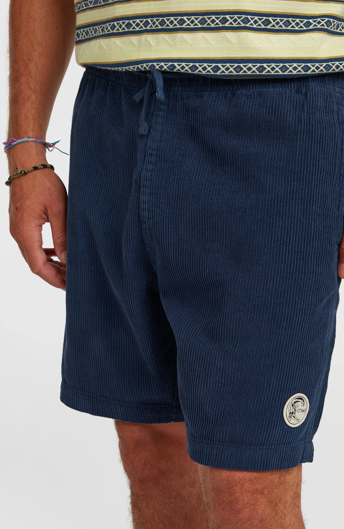 Nahaufnahme der blauen O'Riginals Cord-Shorts am Model mit elastischem Bund und rundem Logo-Badge