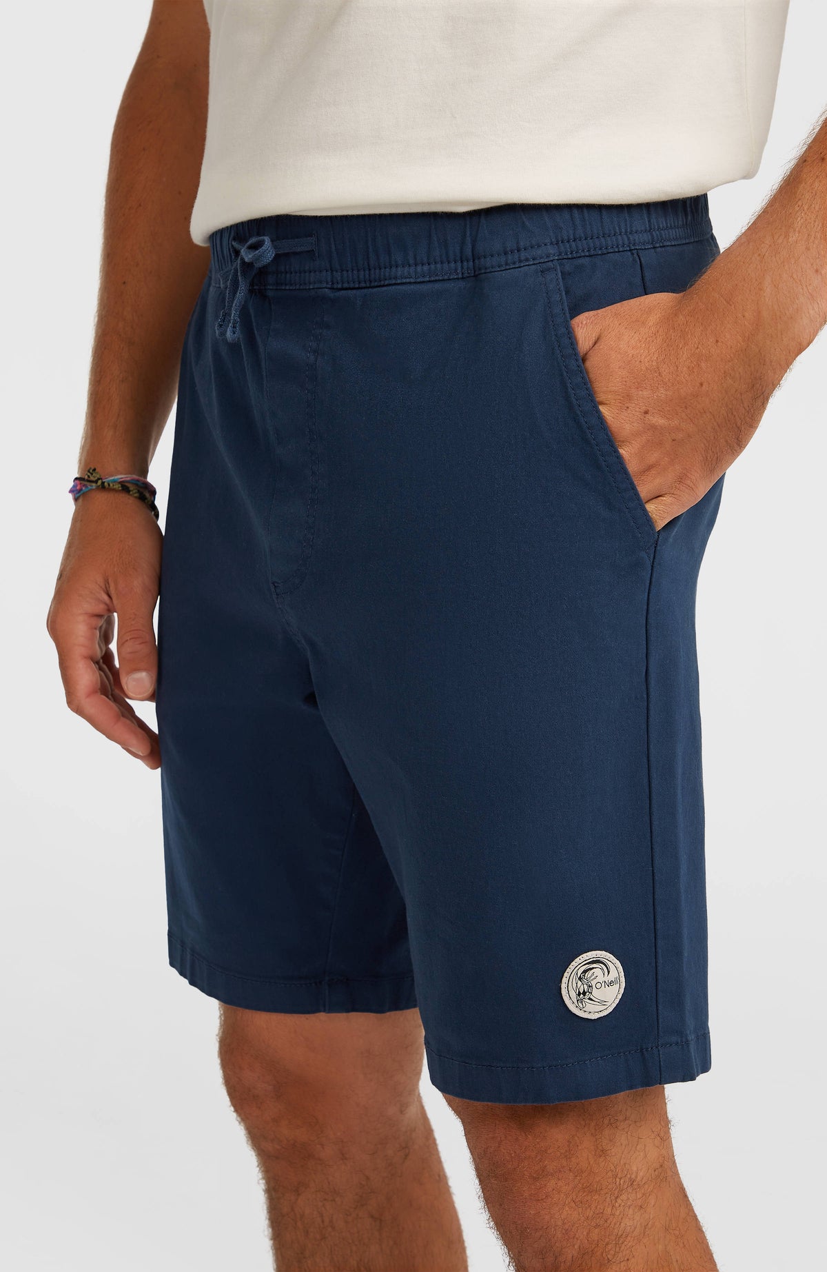O'Riginals Walk Shorts in Blau, Nahaufnahme der Seitentasche und des runden Logo-Aufnähers am Saum