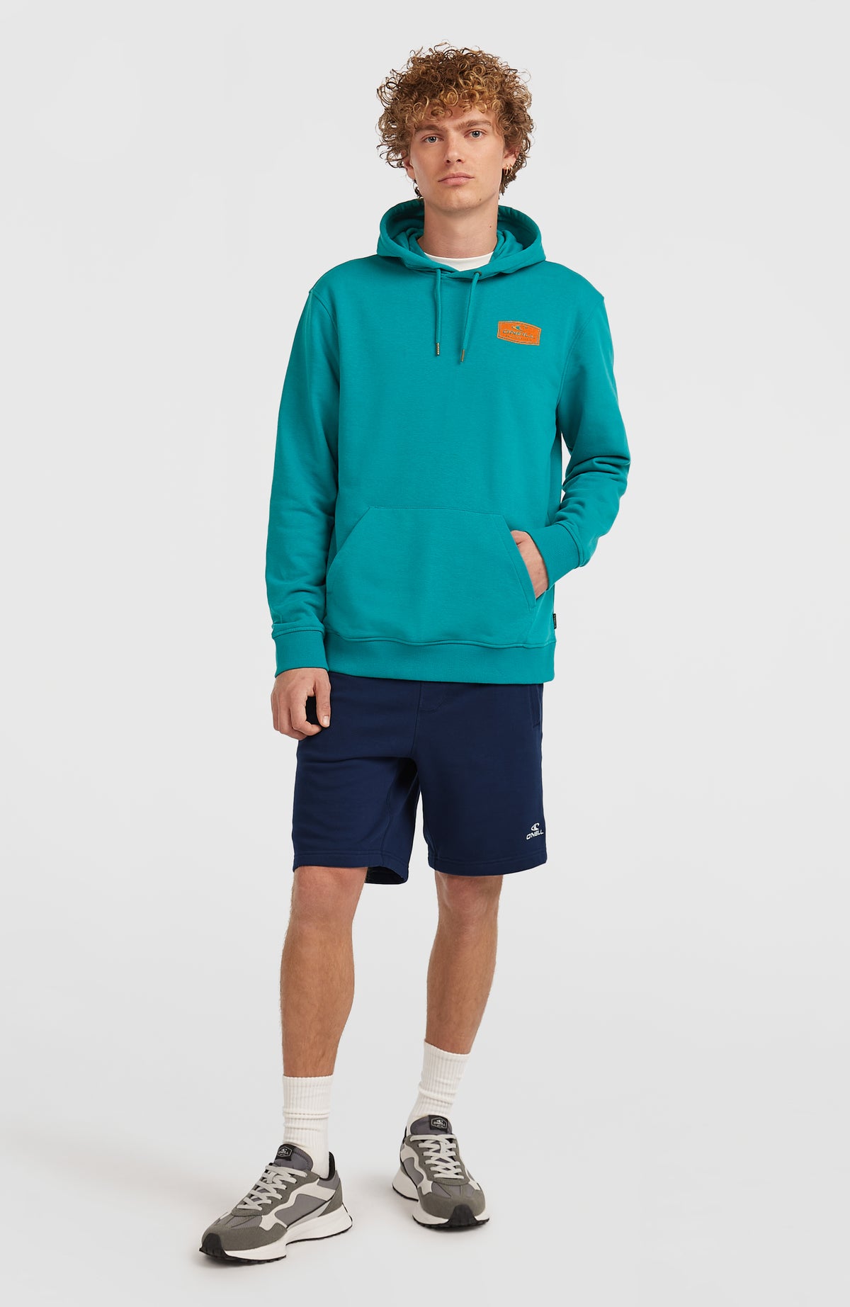 Graphic Hoodie für Herren, blau mit Logo-Patch in Orange, getragen am Model in Ganzkörperansicht