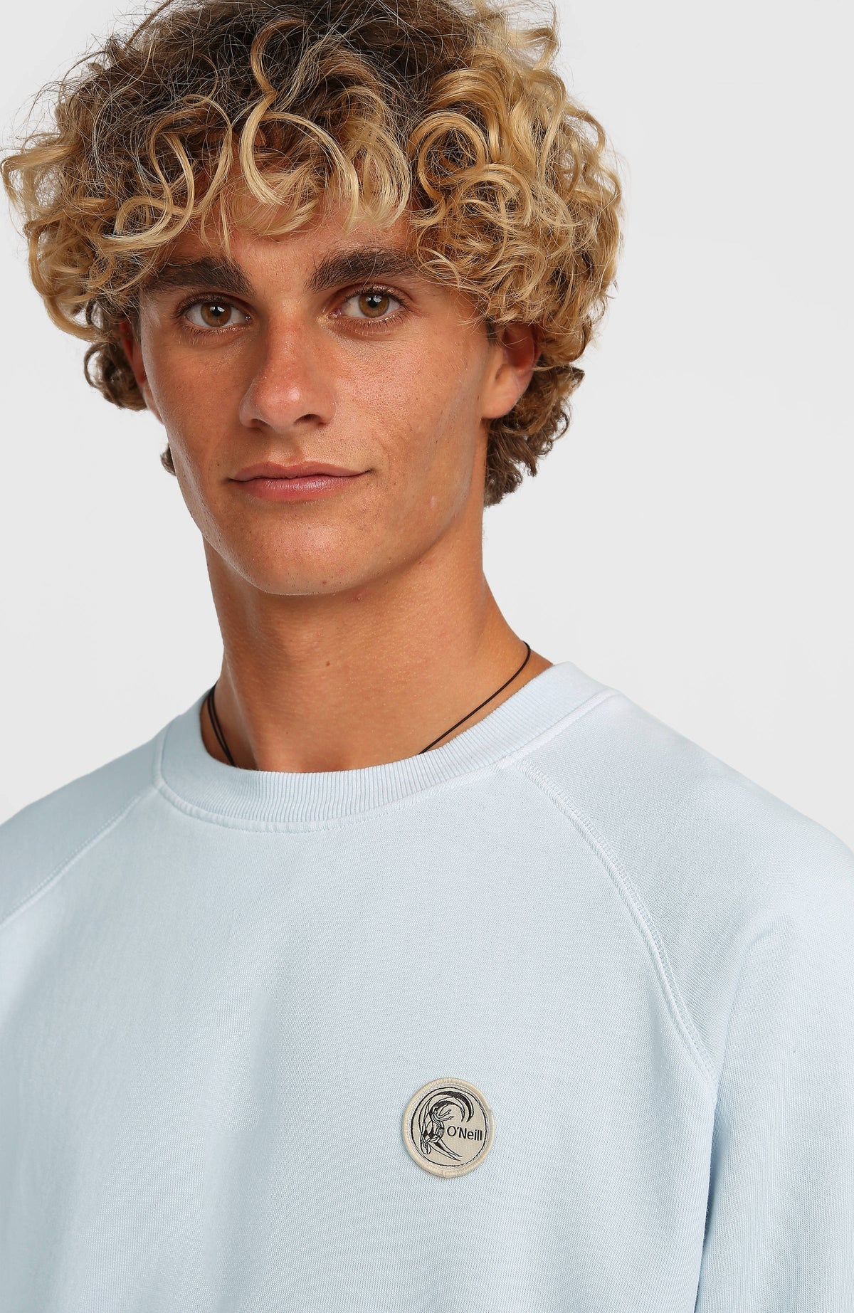 Nahaufnahme am Model von Rundhalsausschnitt und rundem Logo-Badge des blauen O'Riginals Badge Crew Sweatshirts