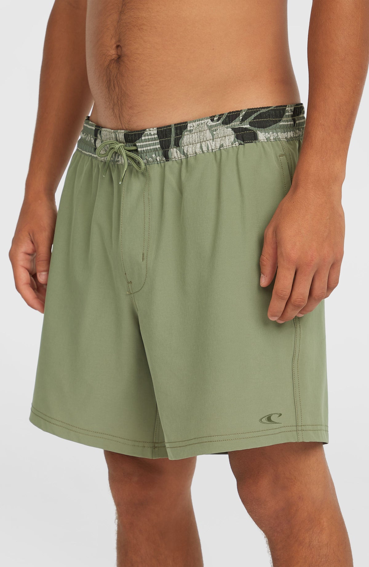 Pocket Print 16'' Badehose für Herren, grün mit Blättermuster, schräge Ansicht am Model mit Logo-Print am Saum
