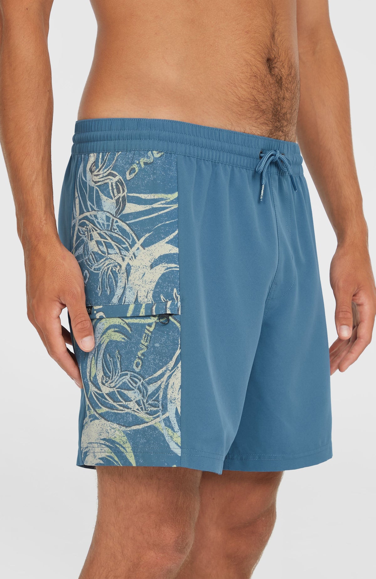 Nahaufnahme der blauen O'Riginals Side Panel 16'' Badehose mit Grafikmuster in Weiß und Reißverschlusstasche