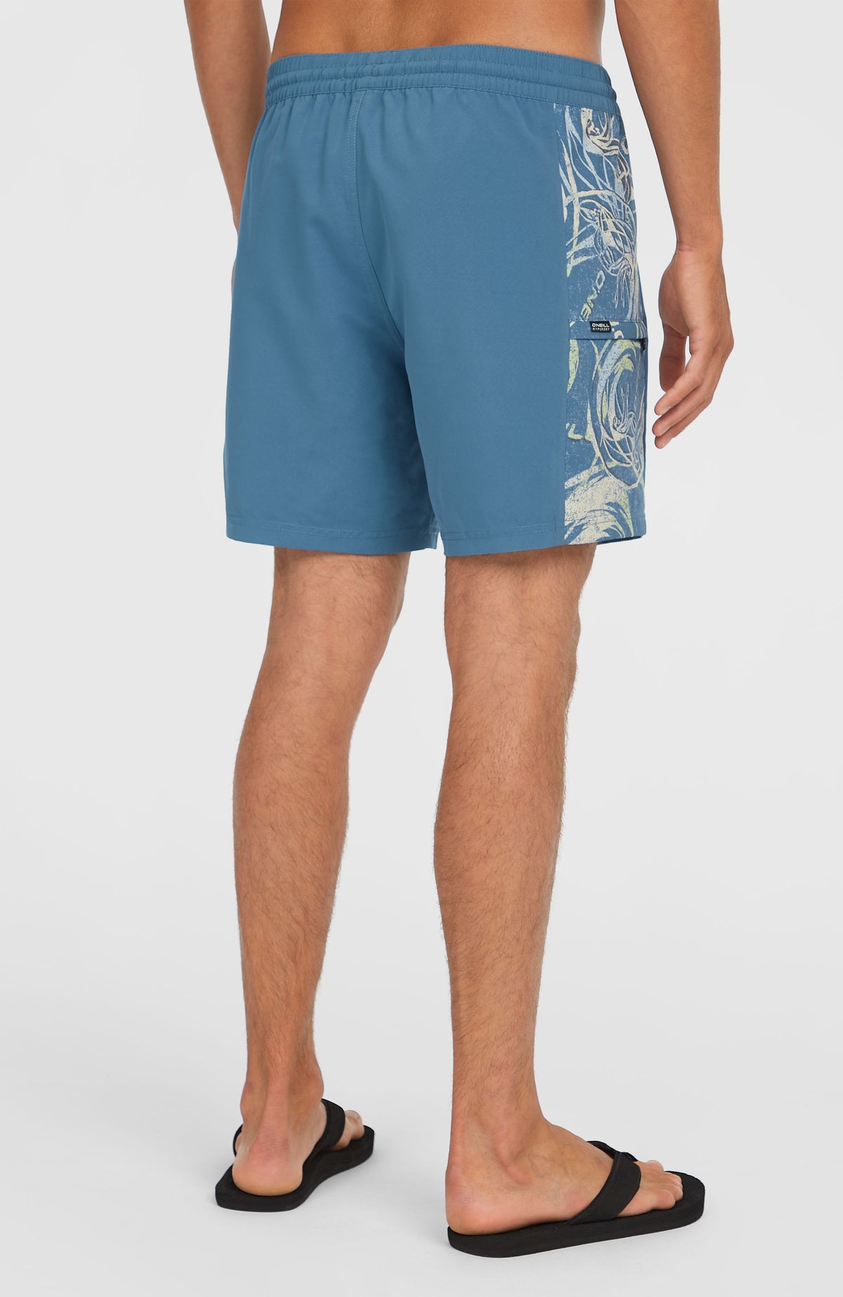 O'Riginals Side Panel 16'' Badehose für Herren, blau mit Grafikmuster in Weiß, halbe Rückansicht am Model