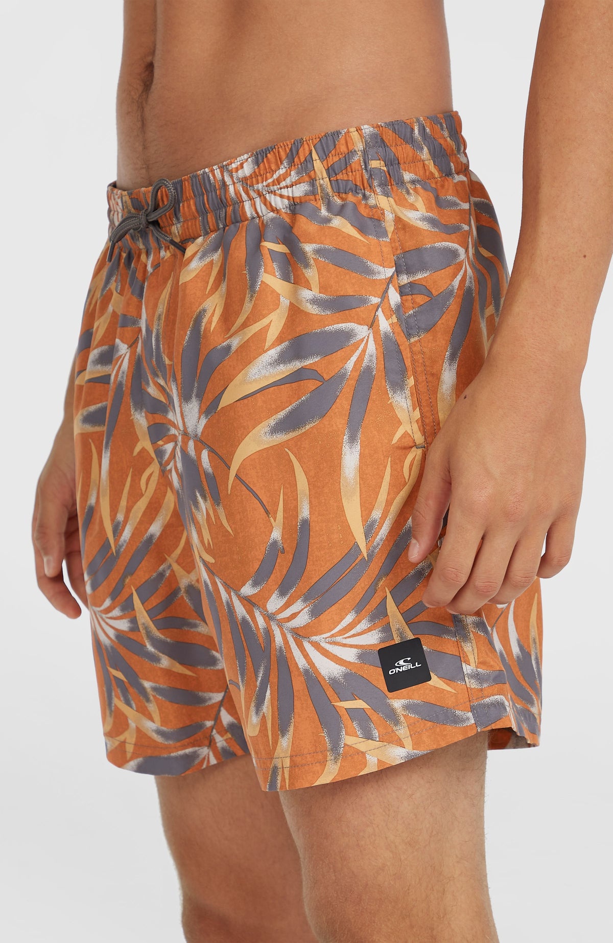 Cali Floral 16'' Badehose, orange mit Blättermuster in Grau, Nahaufnahme der Seite mit Logo-Patch am Saum