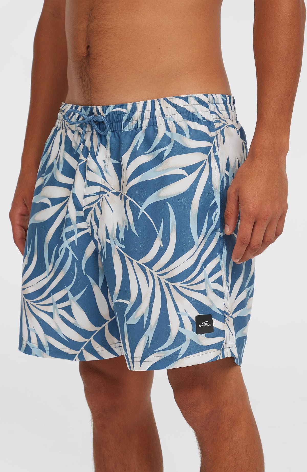 Cali Floral 16'' Badehose für Herren, blau mit Blättermuster in Weiß, Halbansicht am Model mit Logo-Patch