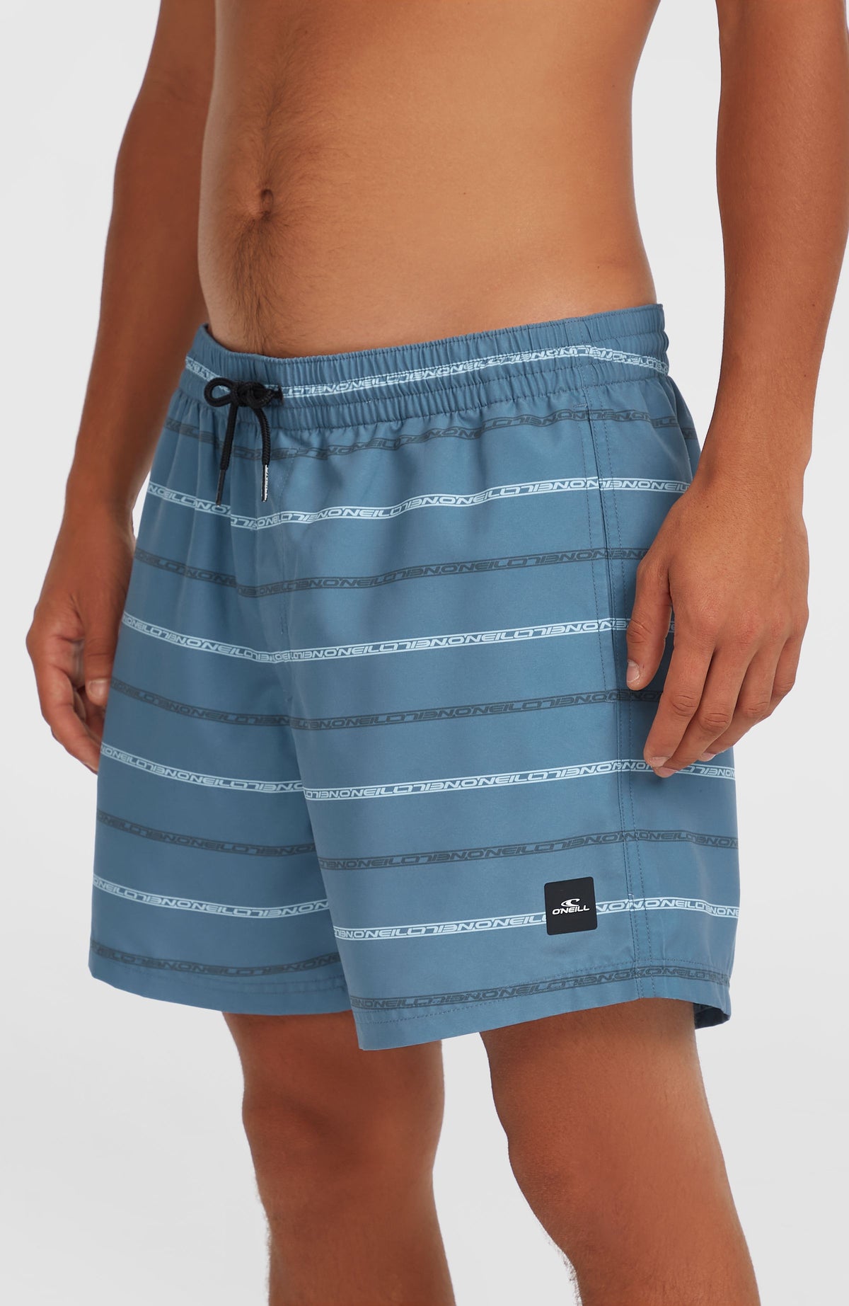 Nahaufnahme der blauen Cali First 15'' Badehose am Model von der Seite mit Logo-Patch am Beinsaum
