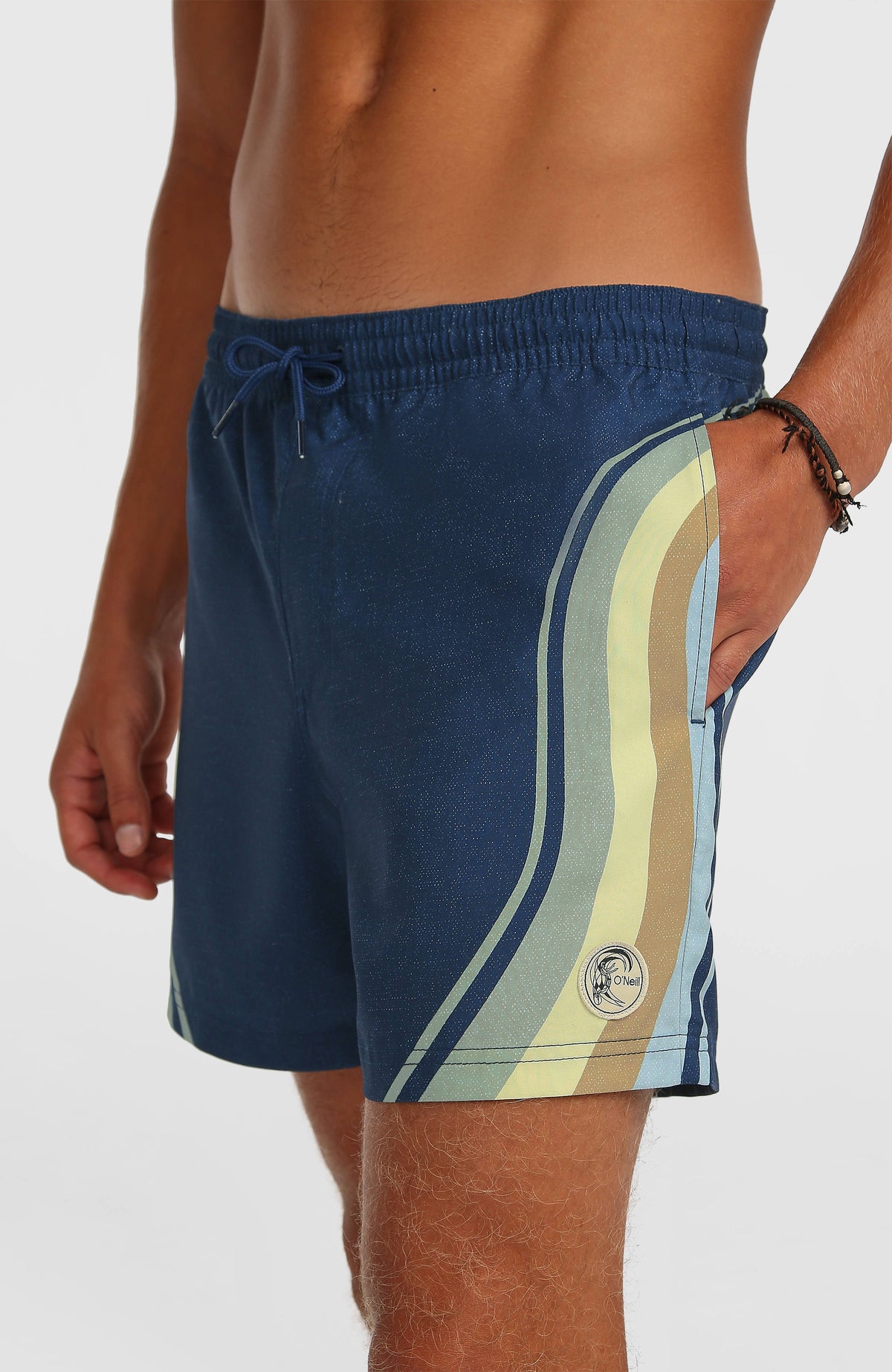 O'Riginals Longboard 15'' Badehose, blau mit Streifenmuster in Gelb und Grün, Nahaufnahme mit Logo-Badge am Saum