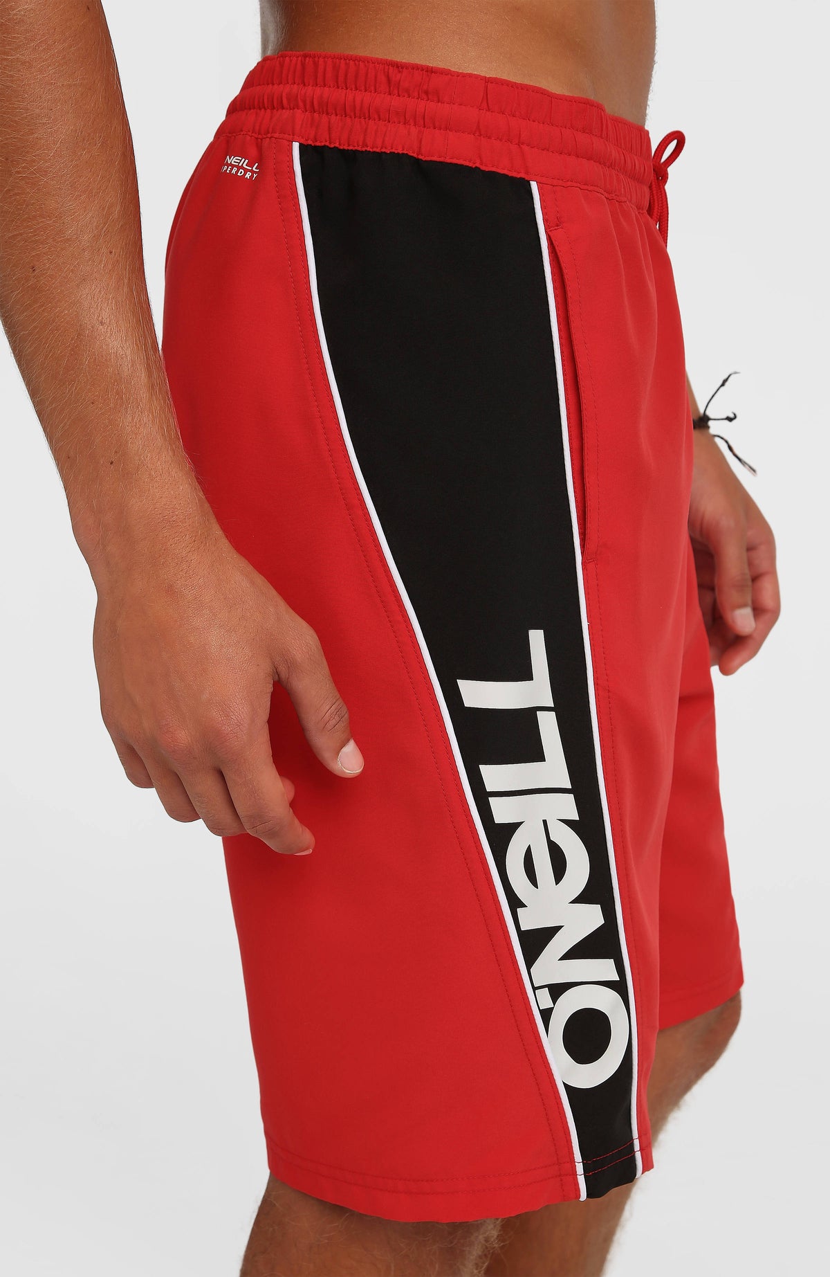 Nahaufnahme des seitlichen Logo-Prints in Schwarz und Weiß an der roten 90s 21'' Badehose am Model