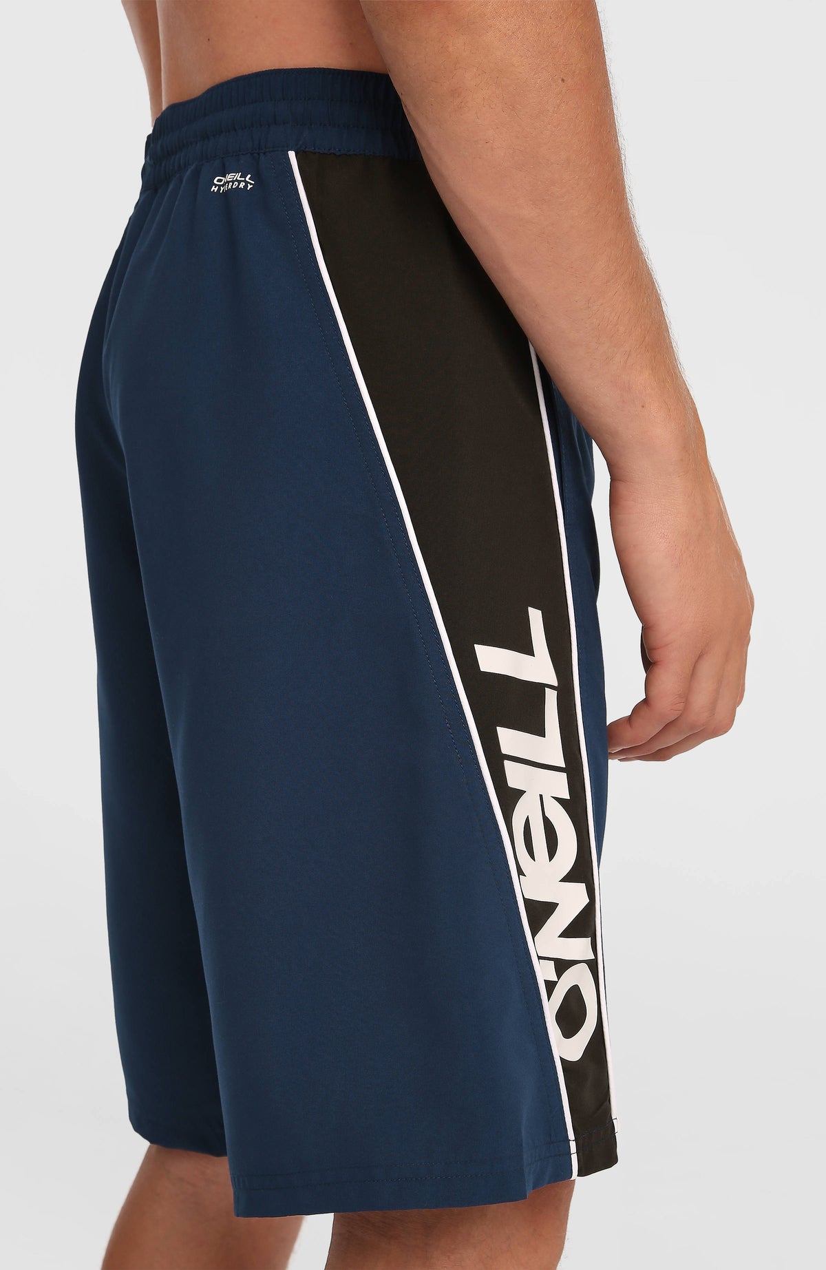 Nahaufnahme des seitlichen Schriftzugs der blauen 90s 21'' Badehose mit Logo-Print in Weiß und Schwarz am Model