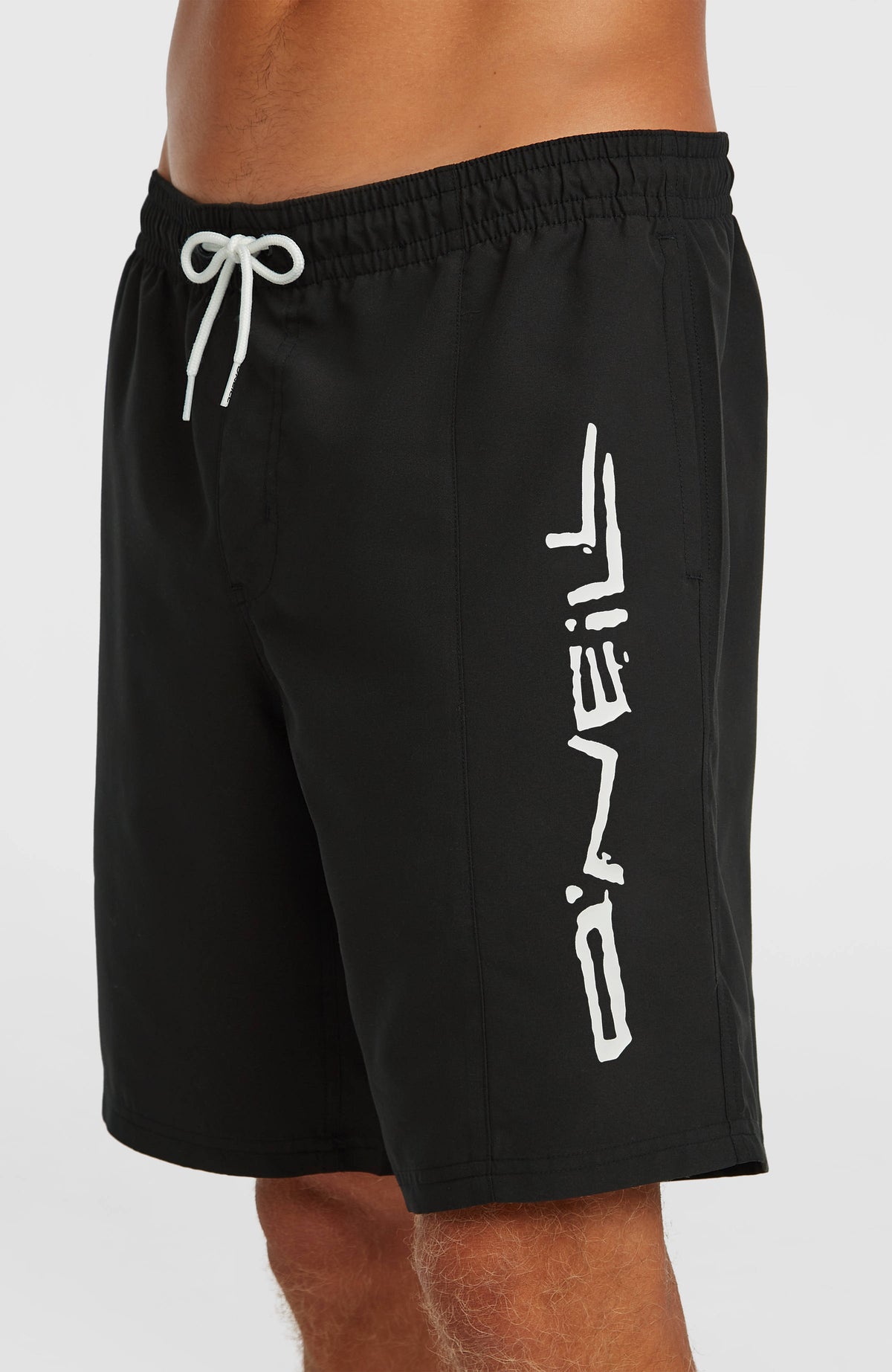 Retro 19'' Badehose für Herren, schwarz mit Logo-Print in Weiß, Nahaufnahme am Model mit Fokus auf das Hosenbein