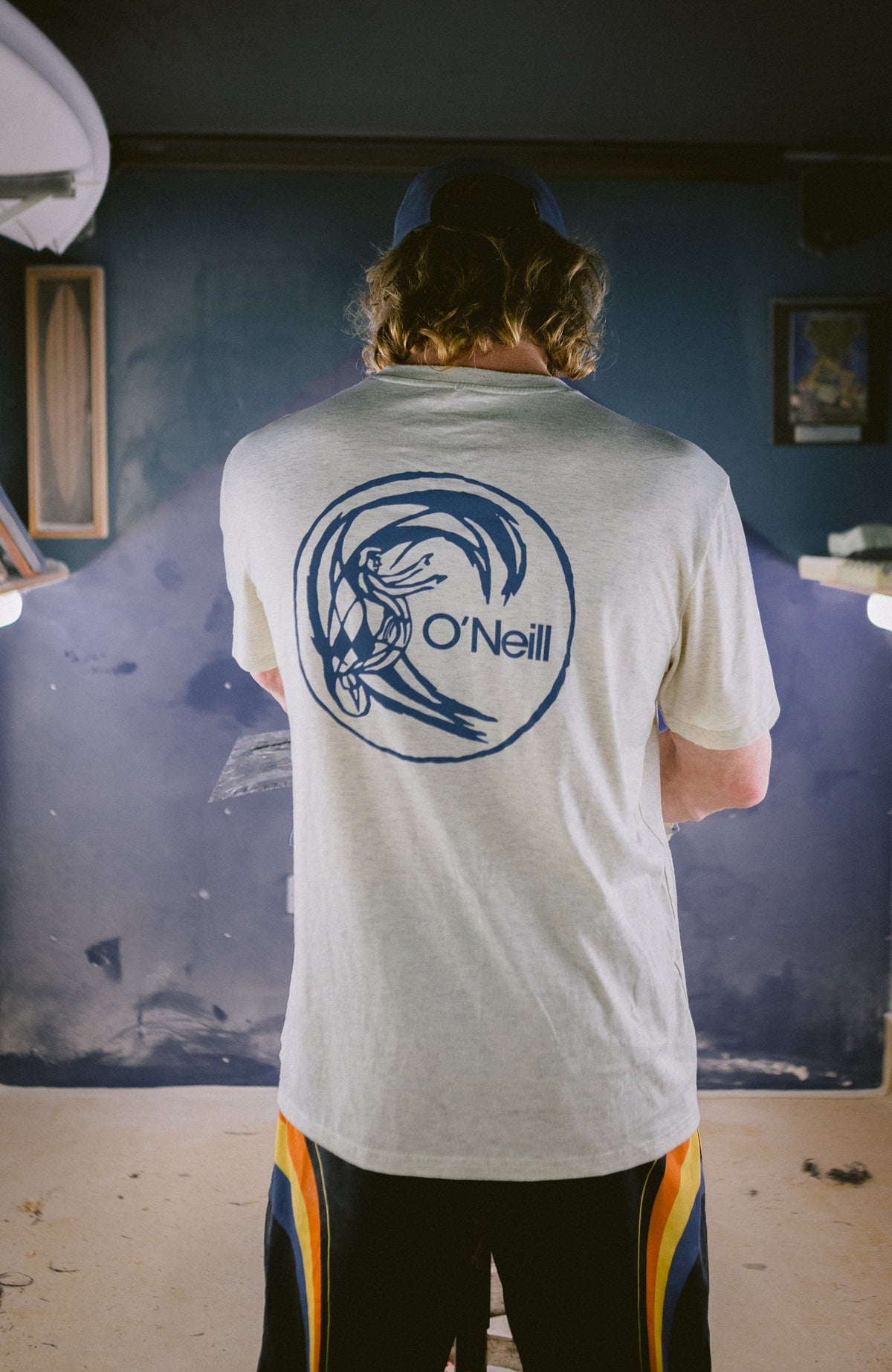 O'Riginals Hybrid T-Shirt, beige mit Logo-Print in Blau, Rückansicht am Model in einer Werkstatt