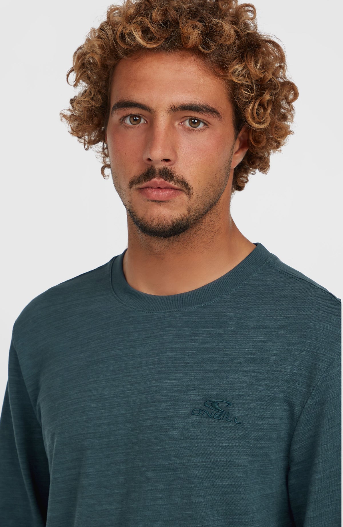 Nahaufnahme von Rundhalsausschnitt und Brustlogo des blauen Slub Langarmshirts für Herren, getragen am Model