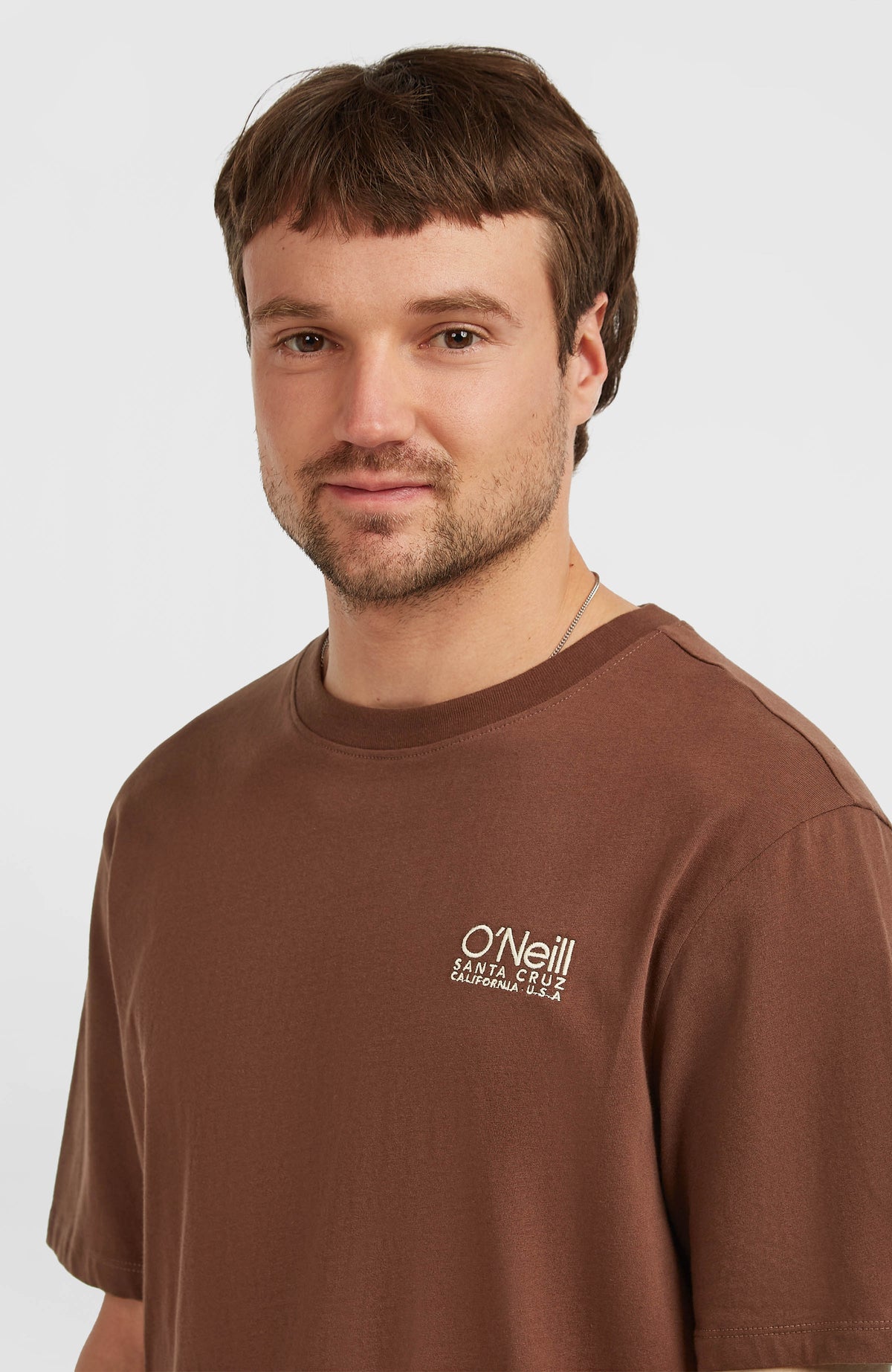 Original Cali Logo T-Shirt, braun mit Logo-Print in Weiß, Nahaufnahme von Rundhalsausschnitt und Brustbereich am Model