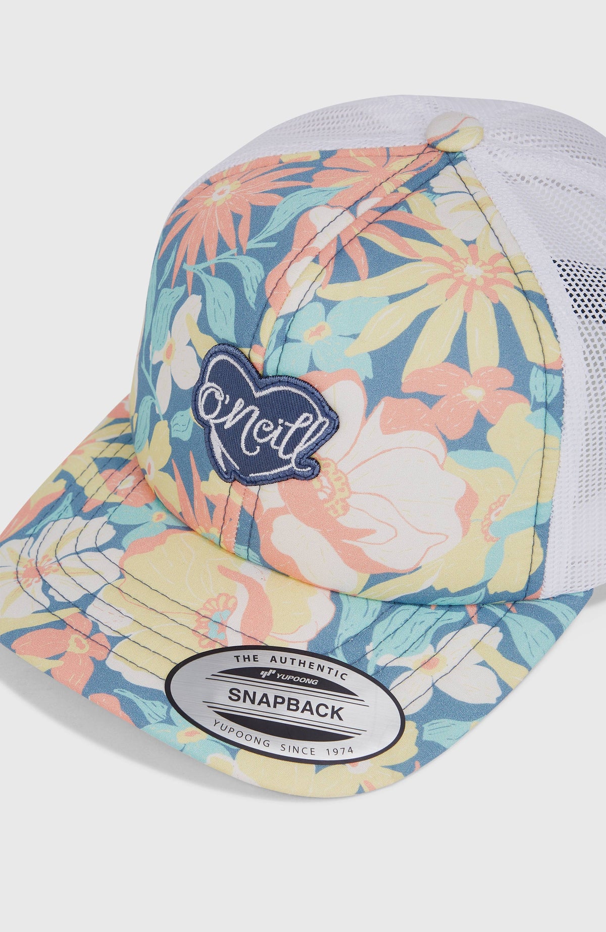 Nahaufnahme der blauen Flood Trucker Cap mit Blumenmuster in Gelb und Rosa, herzförmiger Logo-Aufnäher vorne