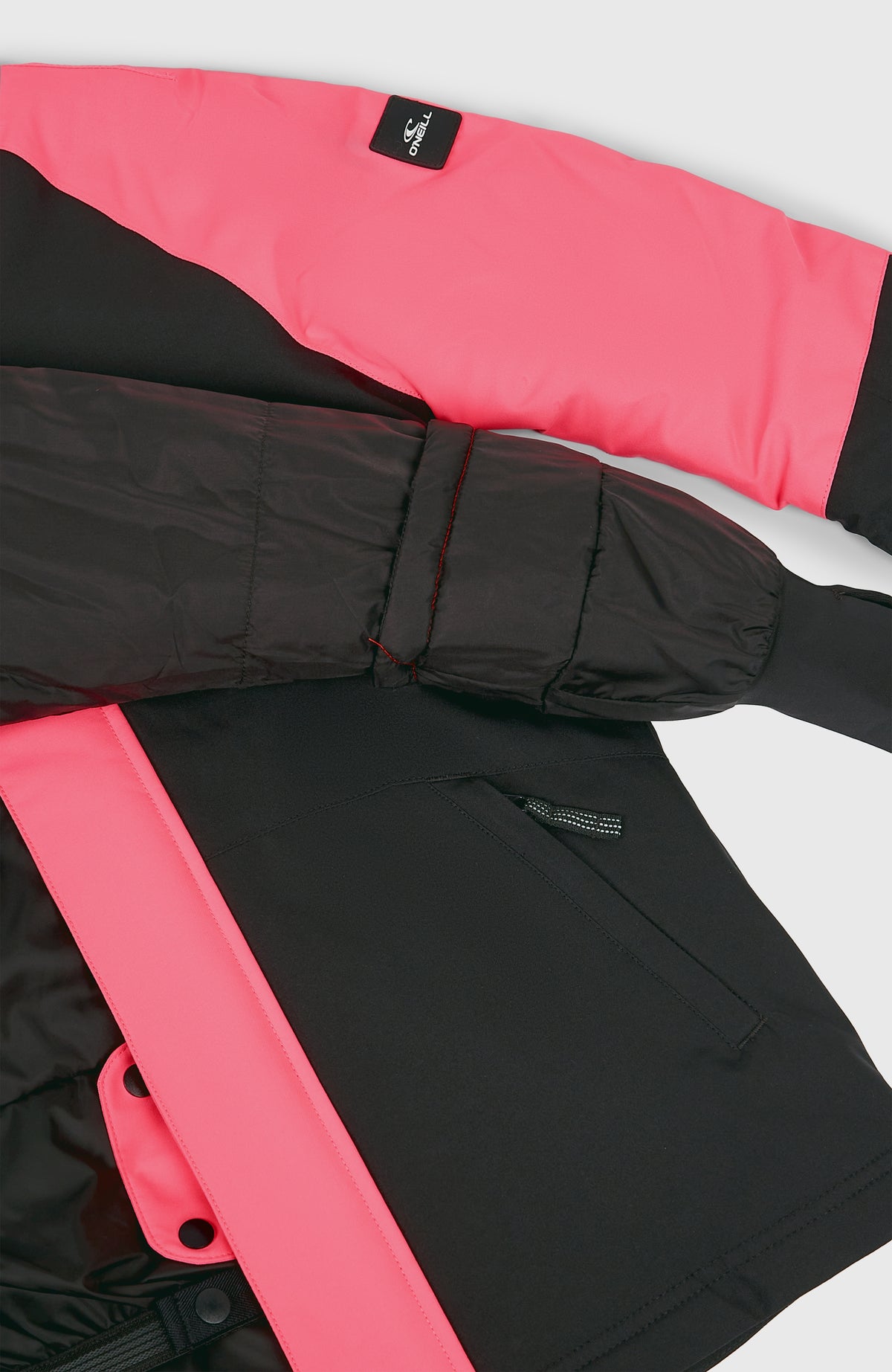 Nahaufnahme der schwarzen FWC'Play Ski- und Snowboardjacke, flach liegend mit Ärmelbündchen und Tasche