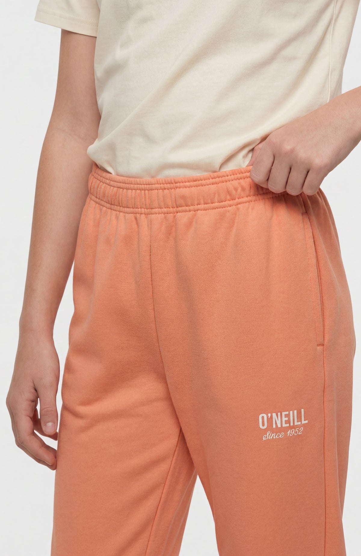 Essentials Jogginghose für Mädchen, orange, Nahaufnahme von elastischem Bund und Seitentasche am Model