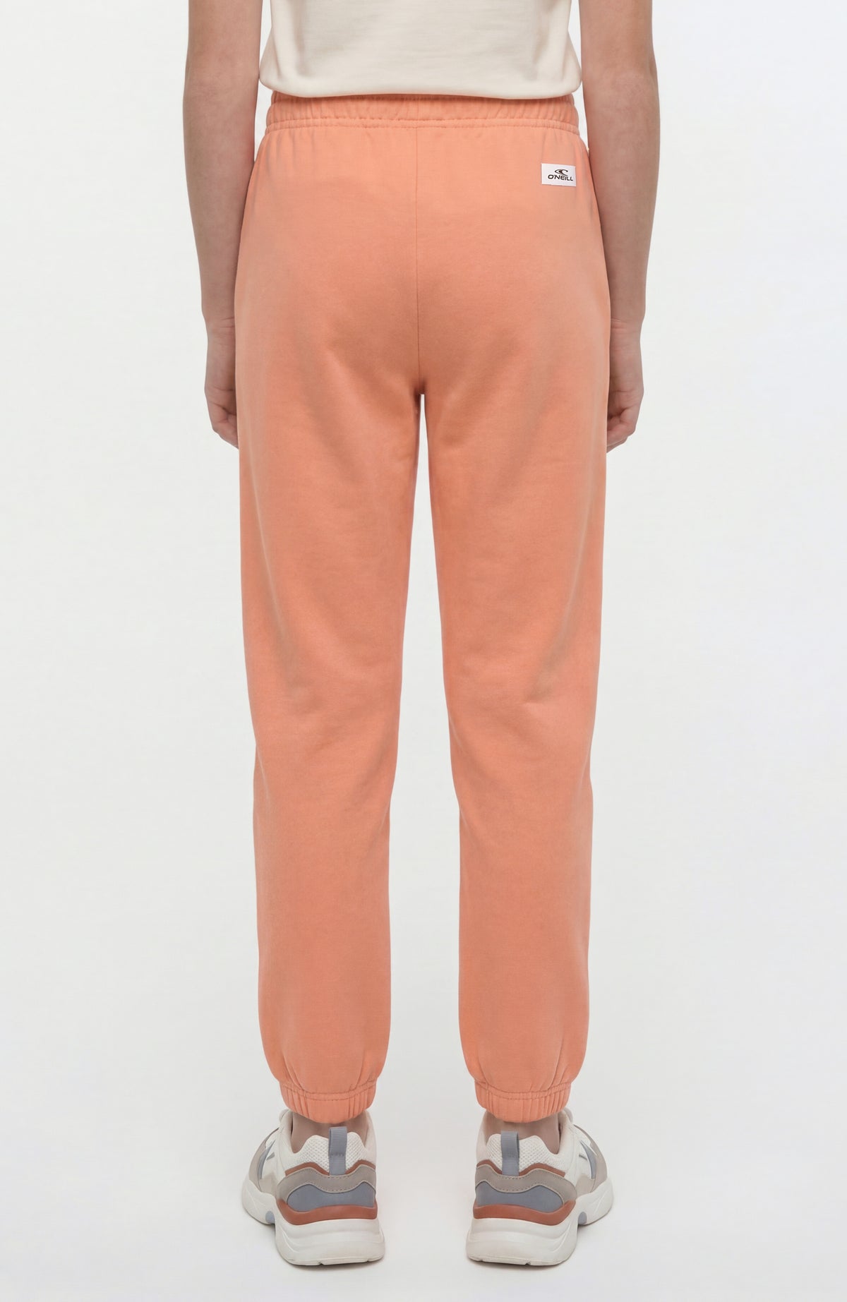 Essentials Jogginghose für Mädchen, orange, Rückansicht am Model mit weißem Logo-Aufnäher am Bund