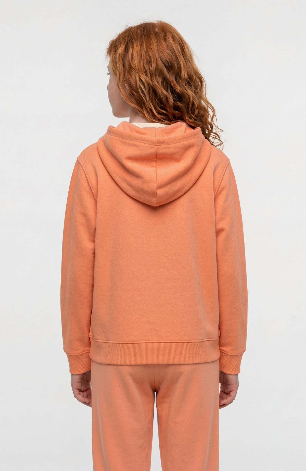 Essentials Hoodie für Mädchen, orange mit Logo-Print in Weiß, Rückansicht getragen am Model