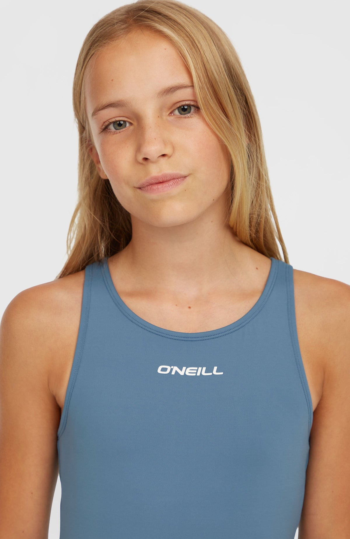 Essentials Badeanzug für Mädchen, blau, Nahaufnahme des Ausschnitts mit weißem Logo-Print, am Model
